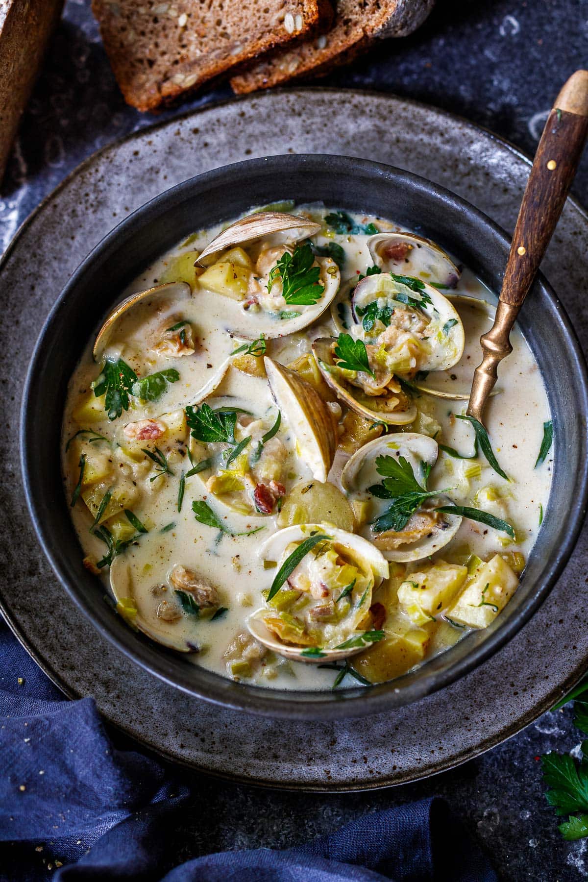 bowl of chowder with clams in shells, bacon bits, fresh herbs, leeks, potatoes