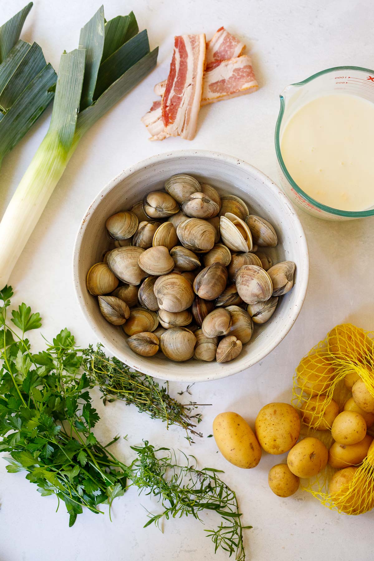 bowl of clams surrounded by ingredients to make clam chowder