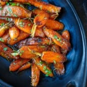glazed carrots garnished with fresh herbs in a serving dish.