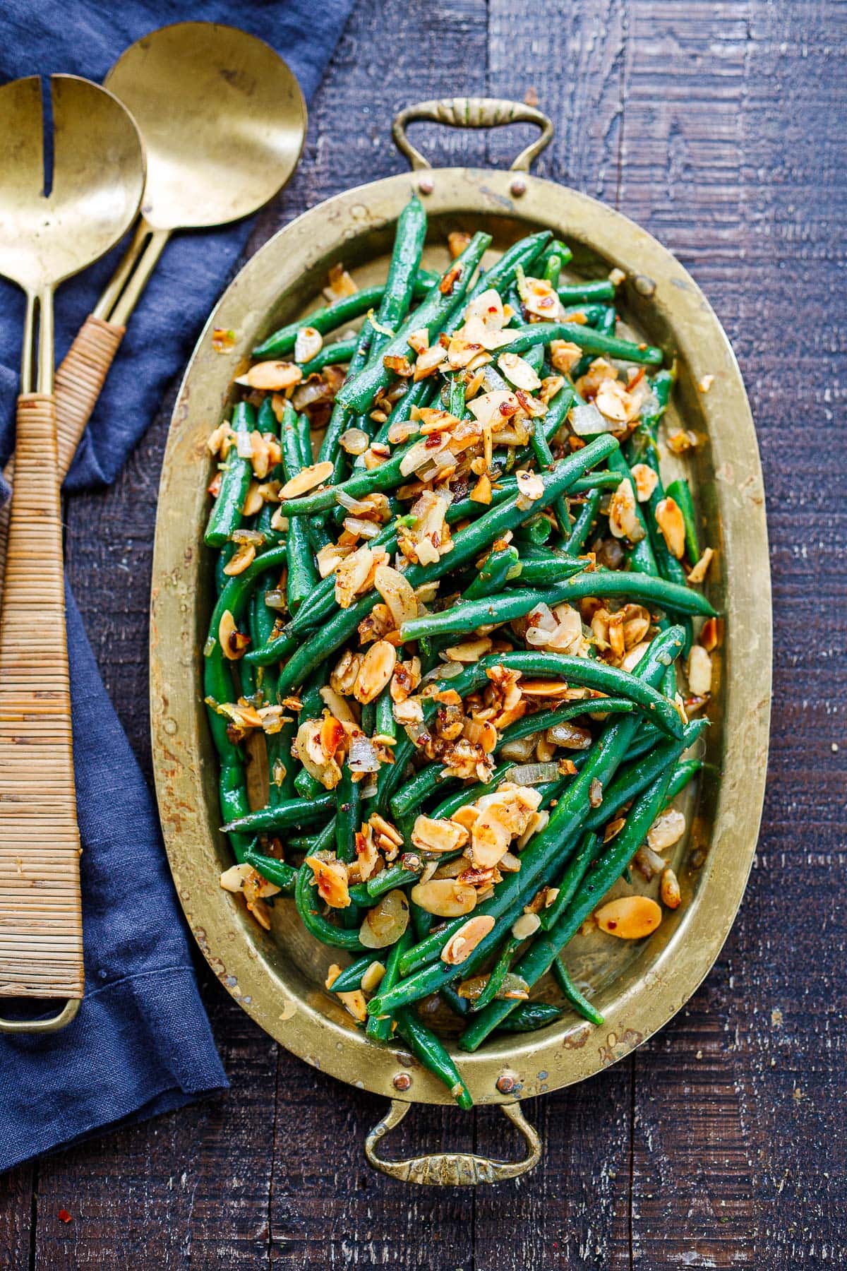 green beans almondine in serving dish topped with sliced toasted almonds, chili flakes.