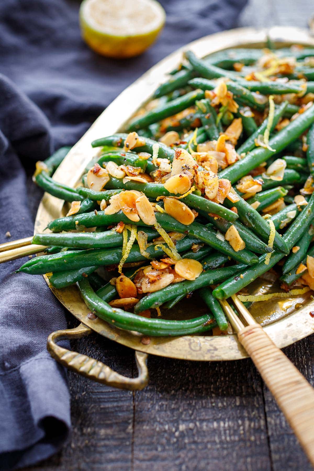 gold serving platter with green beans almondine garnished with toasted almonds, chili flakes, lemon zest