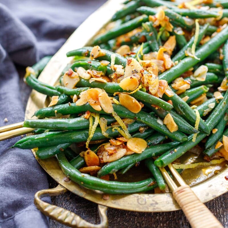 This Green Beans Almondine recipe is so simple yet full of incredible flavor! Toasty almonds, crispy garlic, lemon zest, shallots, and chili pepper flakes bring it up a notch! Vegan.