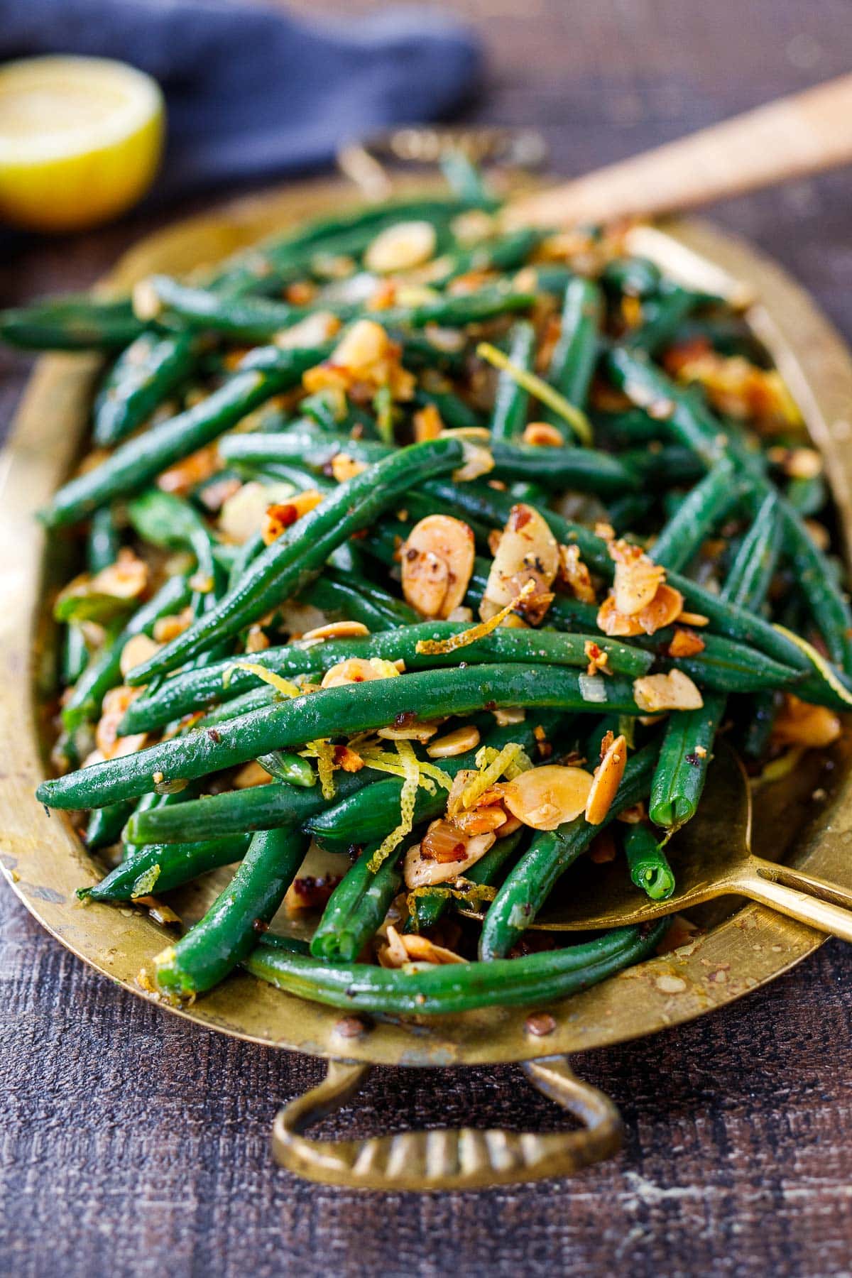 green beans almondine in gold platter dish with sliced almonds and lemon zest.