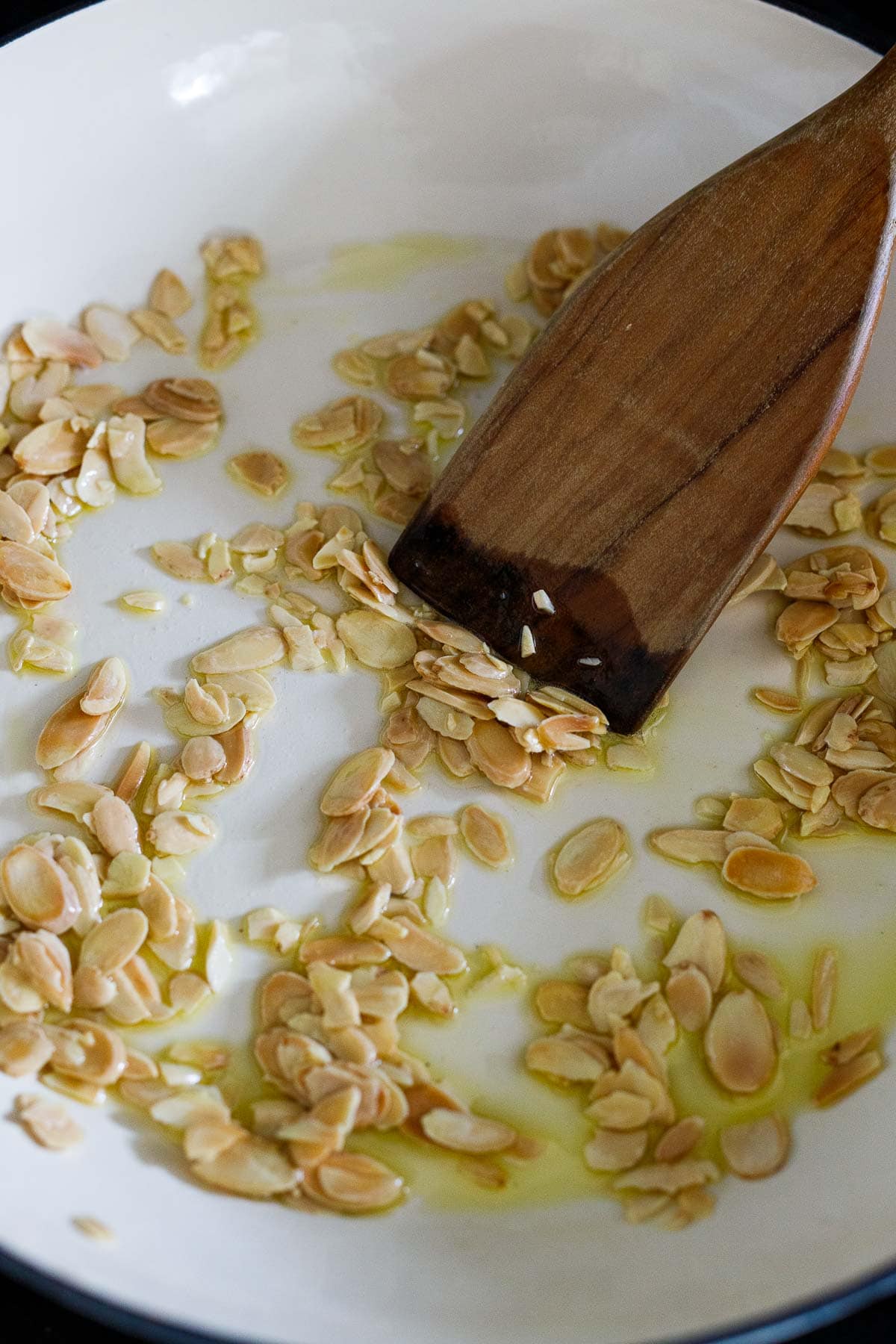 sliced almonds toasting in saute pan with oil and wood spatula