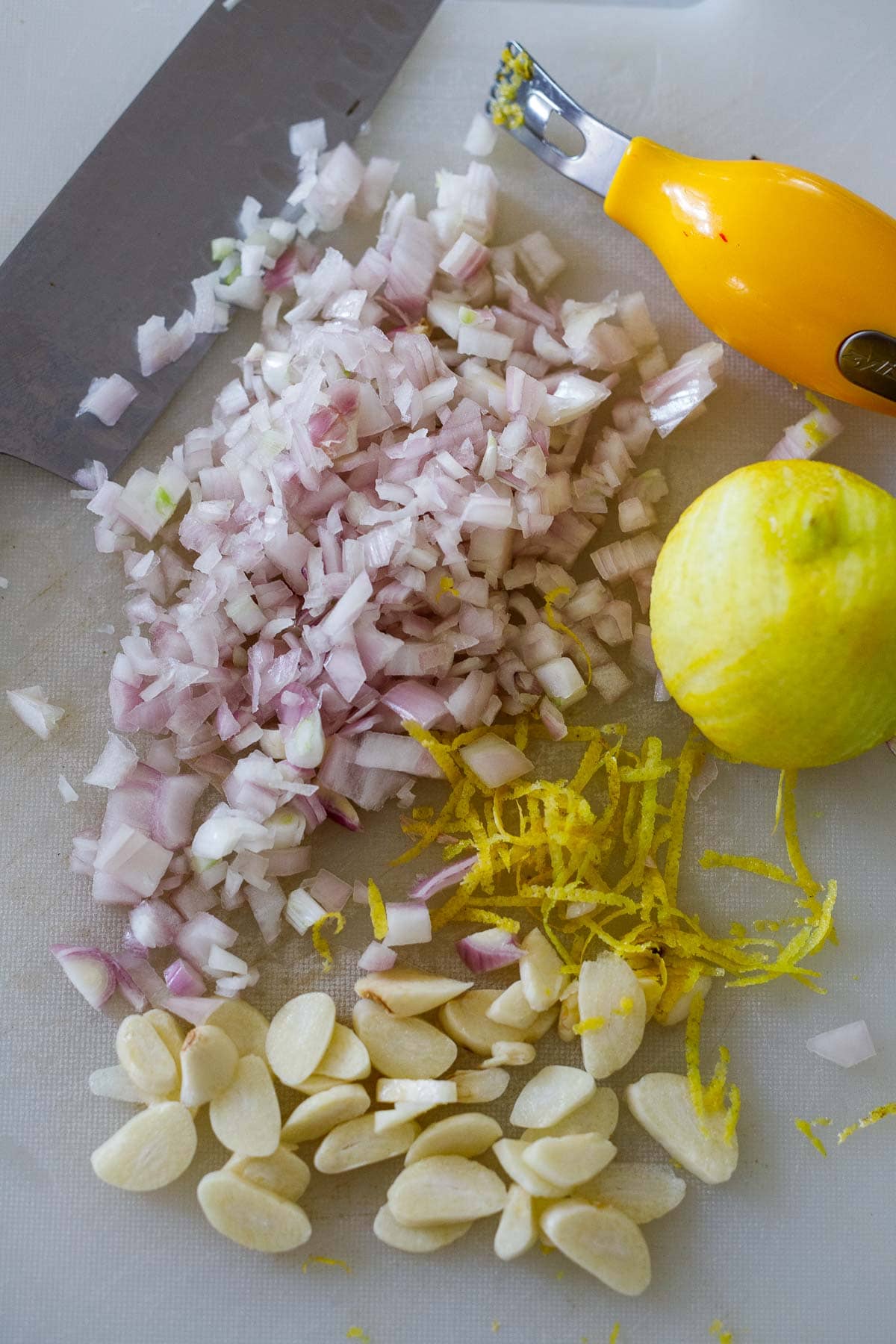 cutting board with knife, chopped shallots, sliced garlic, zested lemon