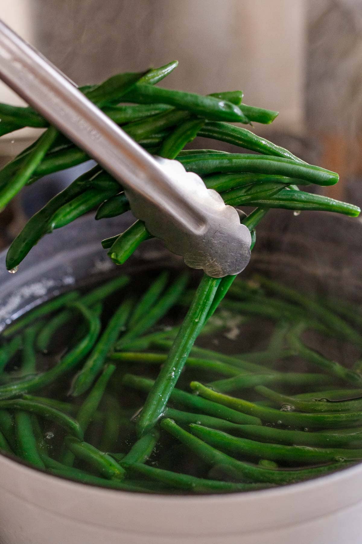 tongs removing blanched green beans from pot of water