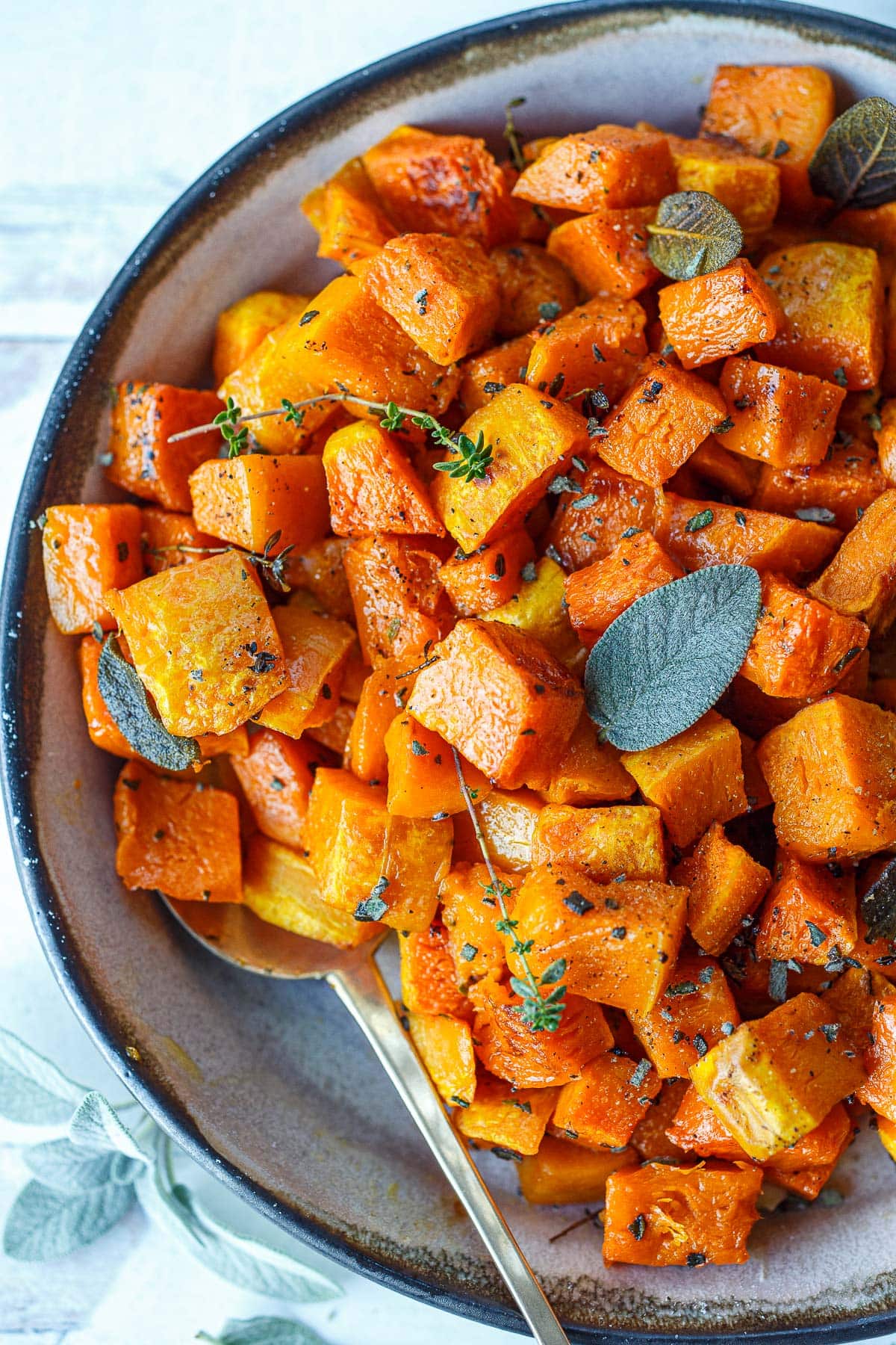 caramelized, roasted butternut squash cubes in bowl with fresh thyme and sage.