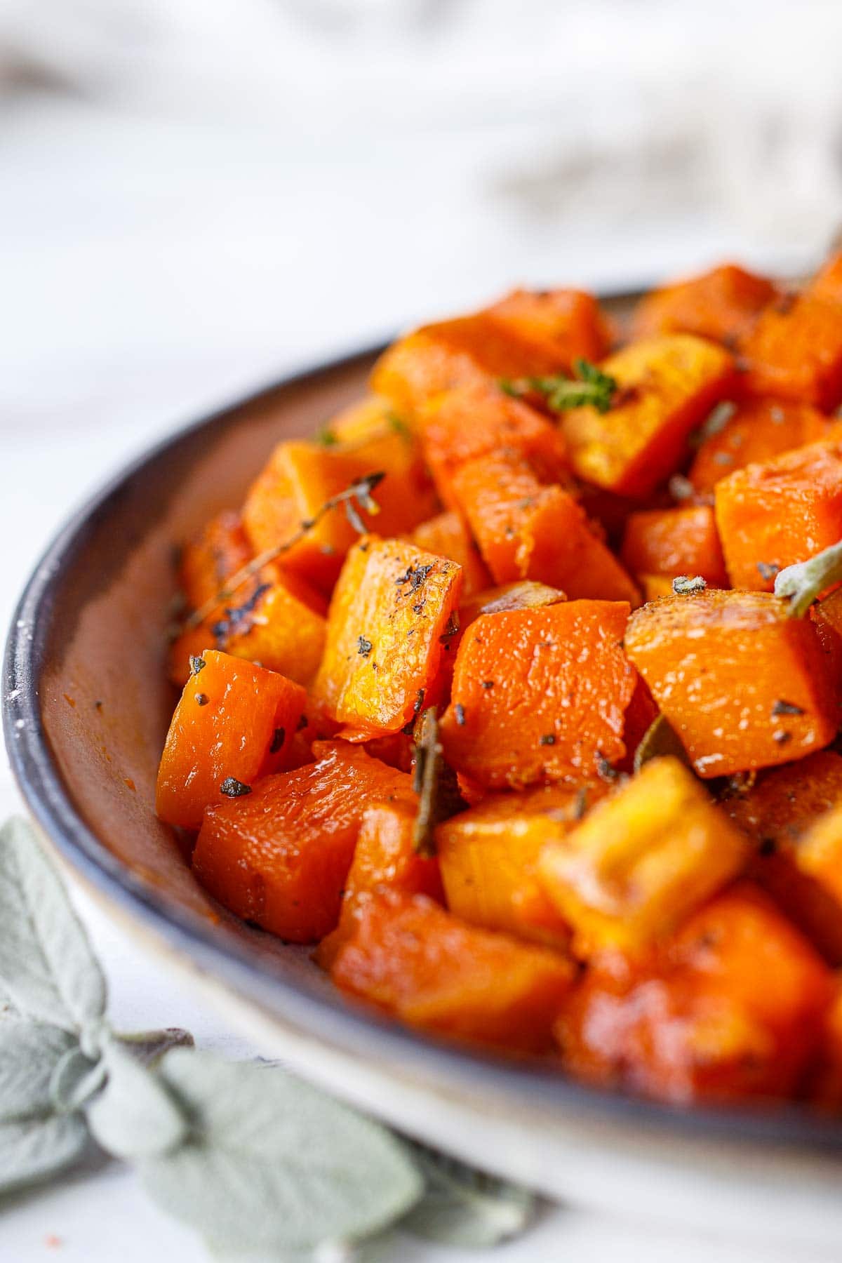 close up of cubed roasted butternut squash in bowl garnished with herbs