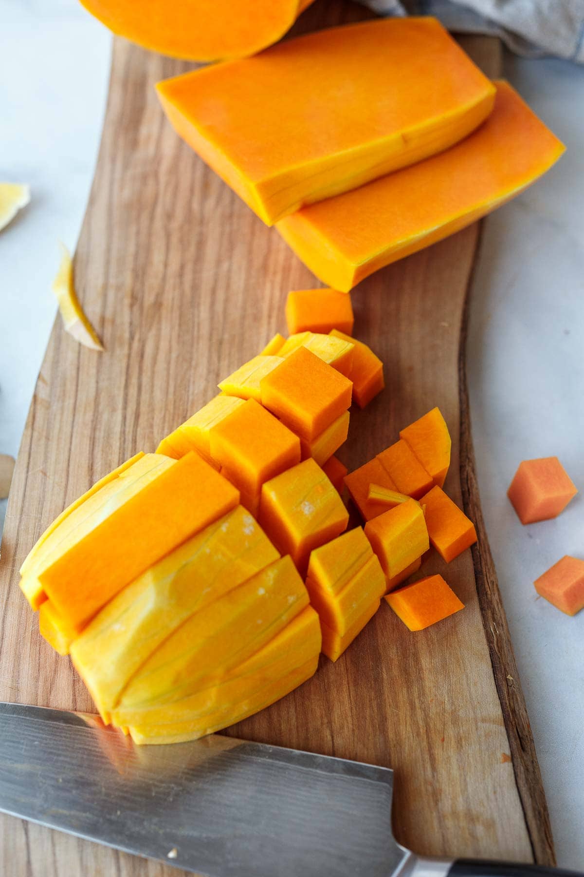 peeled butternut squash cut into even cubes with chef knife on wood cutting board