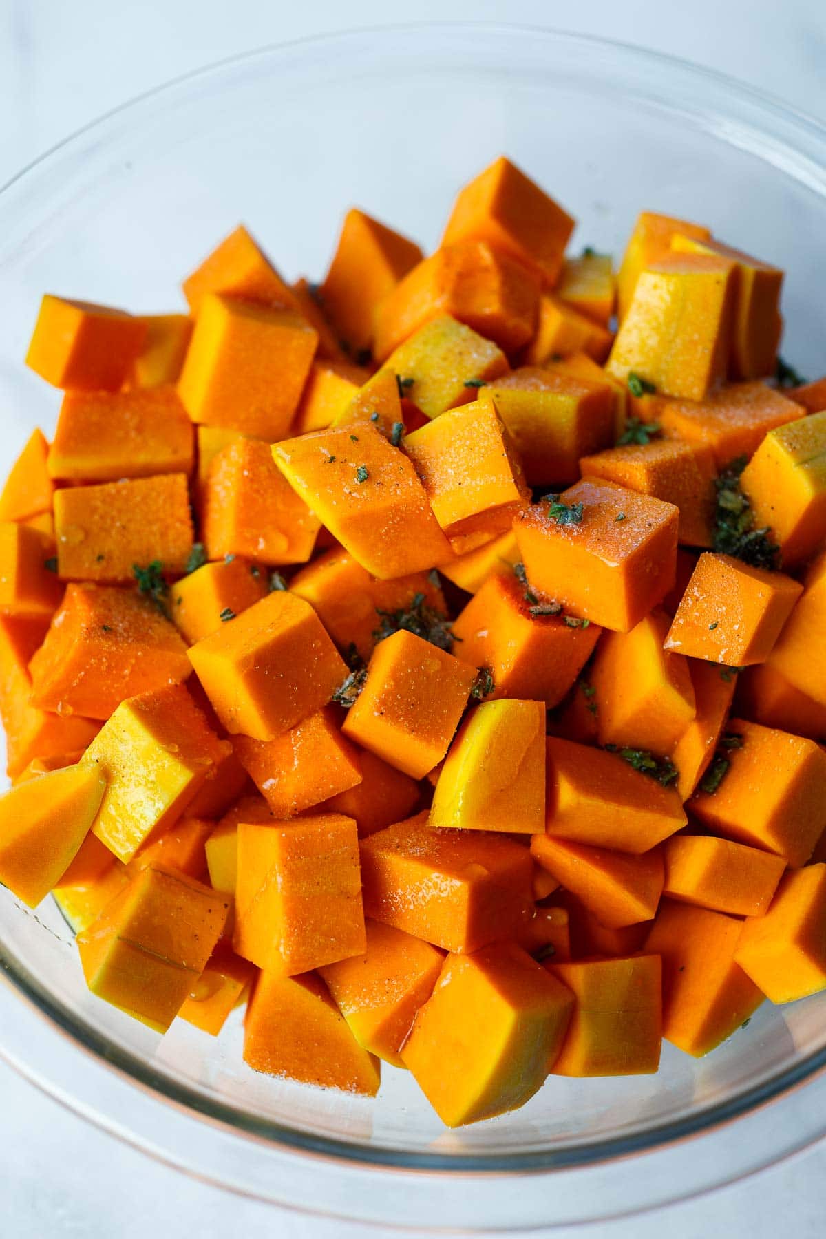 cubed butternut squash in mixing bowl with oil and fresh herbs