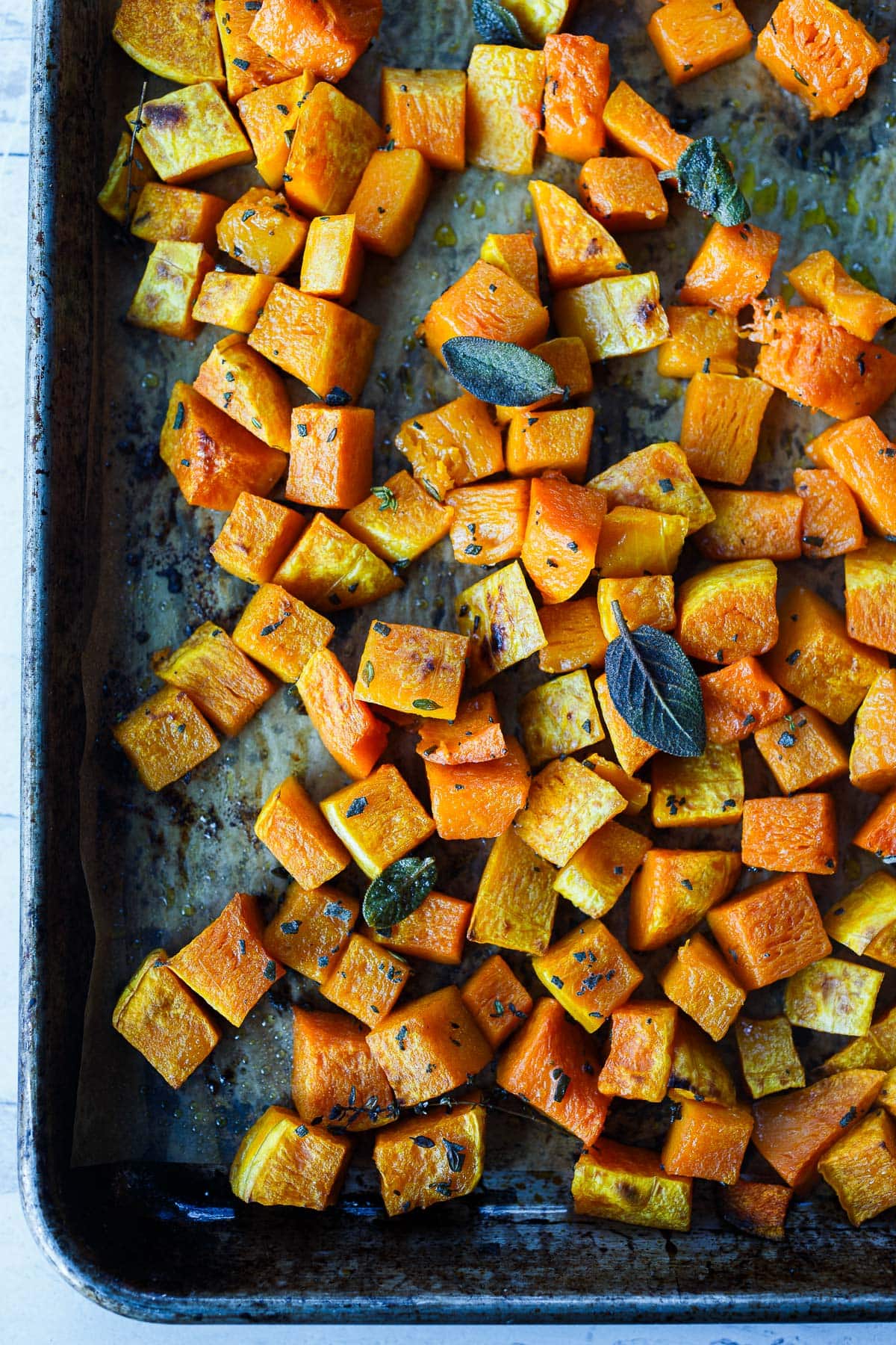 cubed roasted butternut squash on parchment lined baking sheet with caramelized edges and herbs