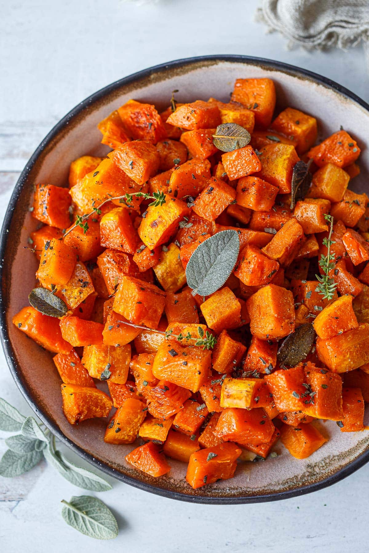 roasted butternut squash in bowl with fresh thyme and sage