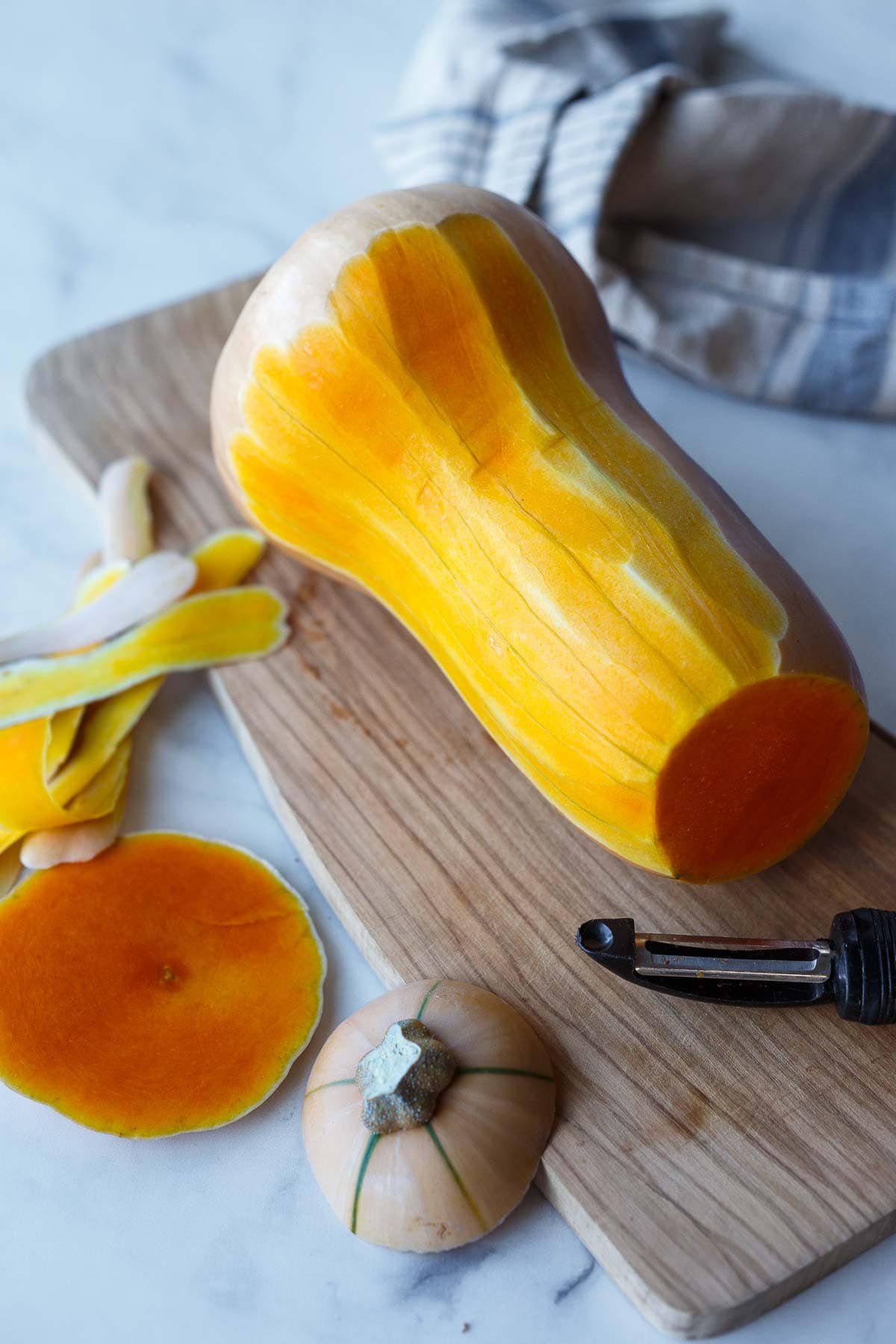 peeling butternut squash with a vegetable peeler on wood cutting board