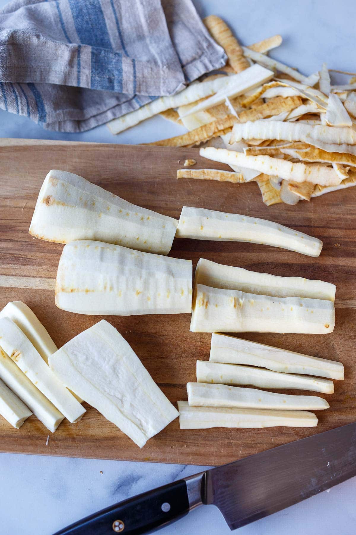 peeling parsnips on wood cutting board with knife