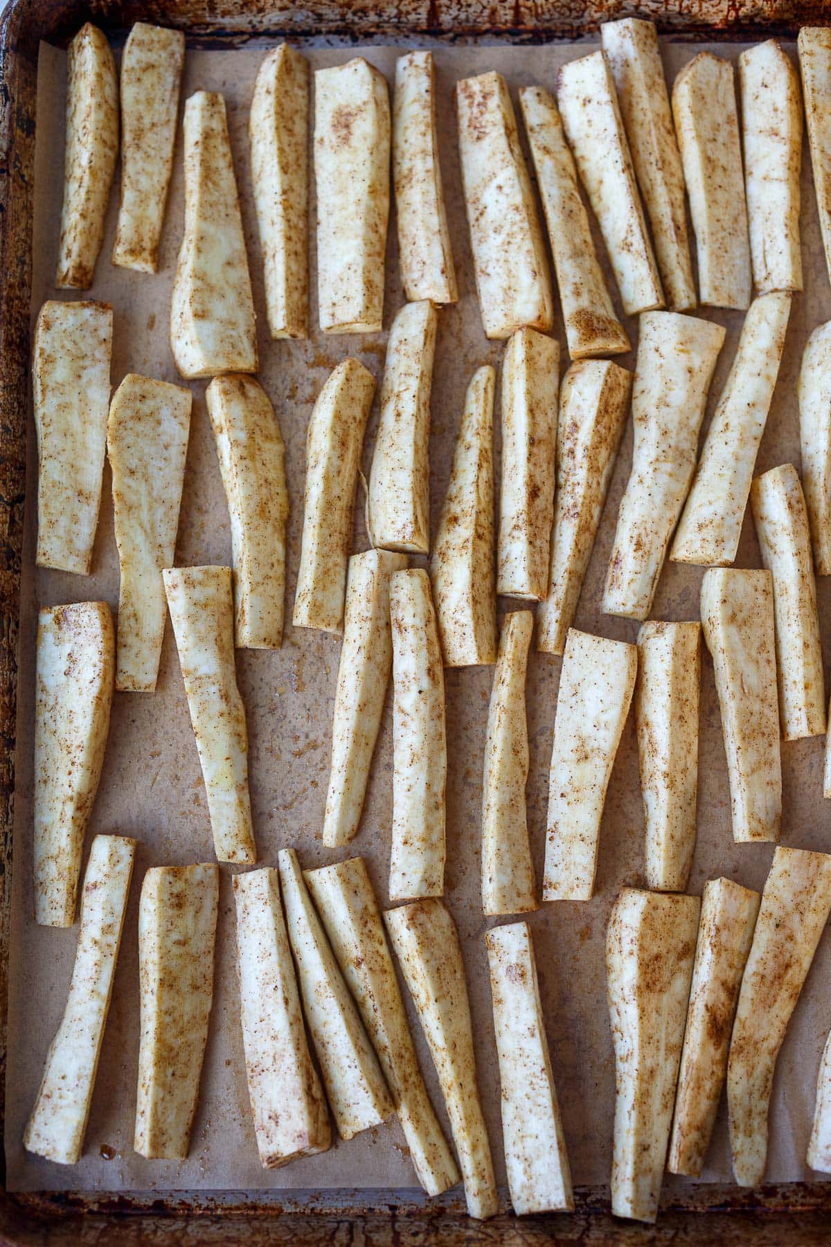 peeled and seasoned parsnips on baking sheet with parchment paper