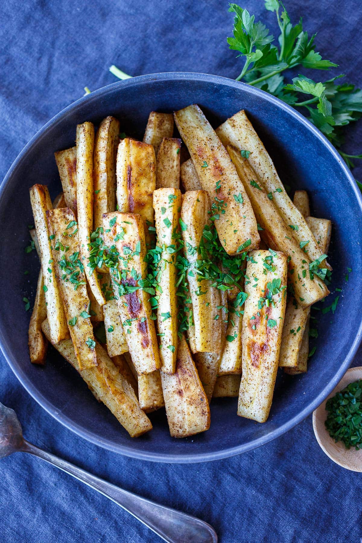 blue serving dish with roasted parsnips garnished with fresh parsley