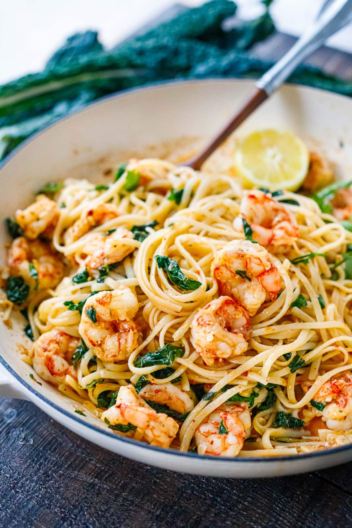 bowl of shrimp pasta in garlic sauce with kale and half of a lemon