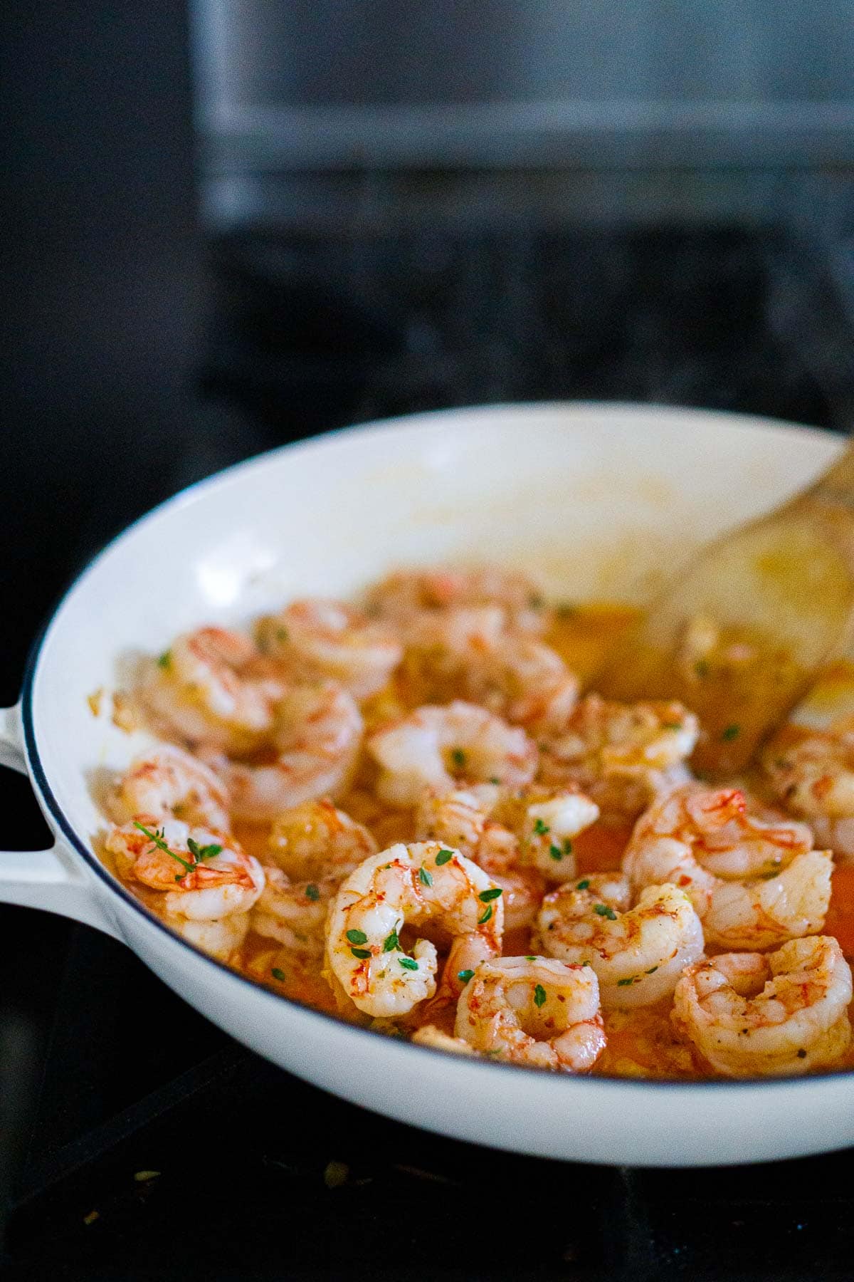 cooking shrimp in saucepan with fresh herbs in garlicky sauce