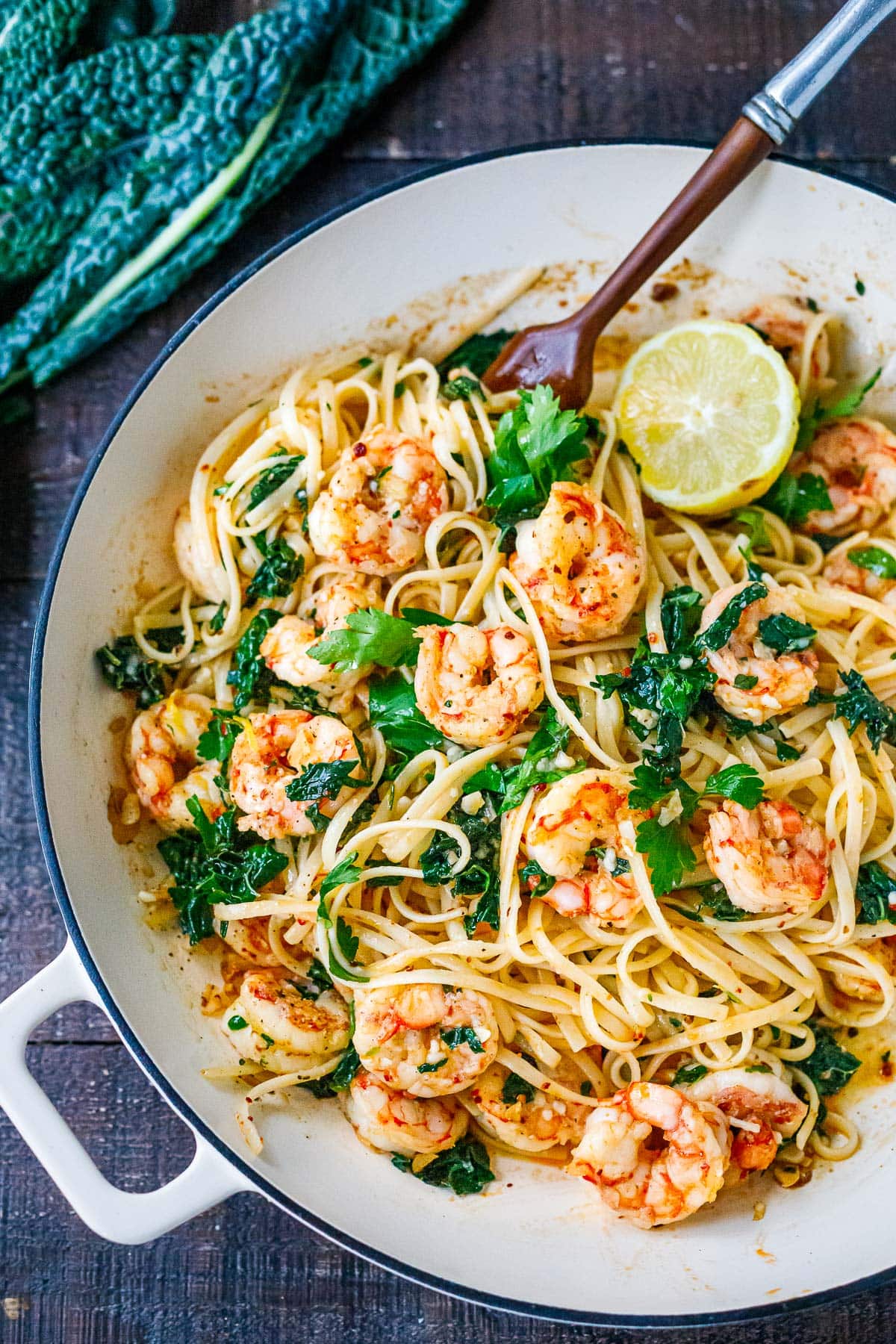 saucepan with shrimp pasta in garlic sauce with wilted kale, sliced lemon