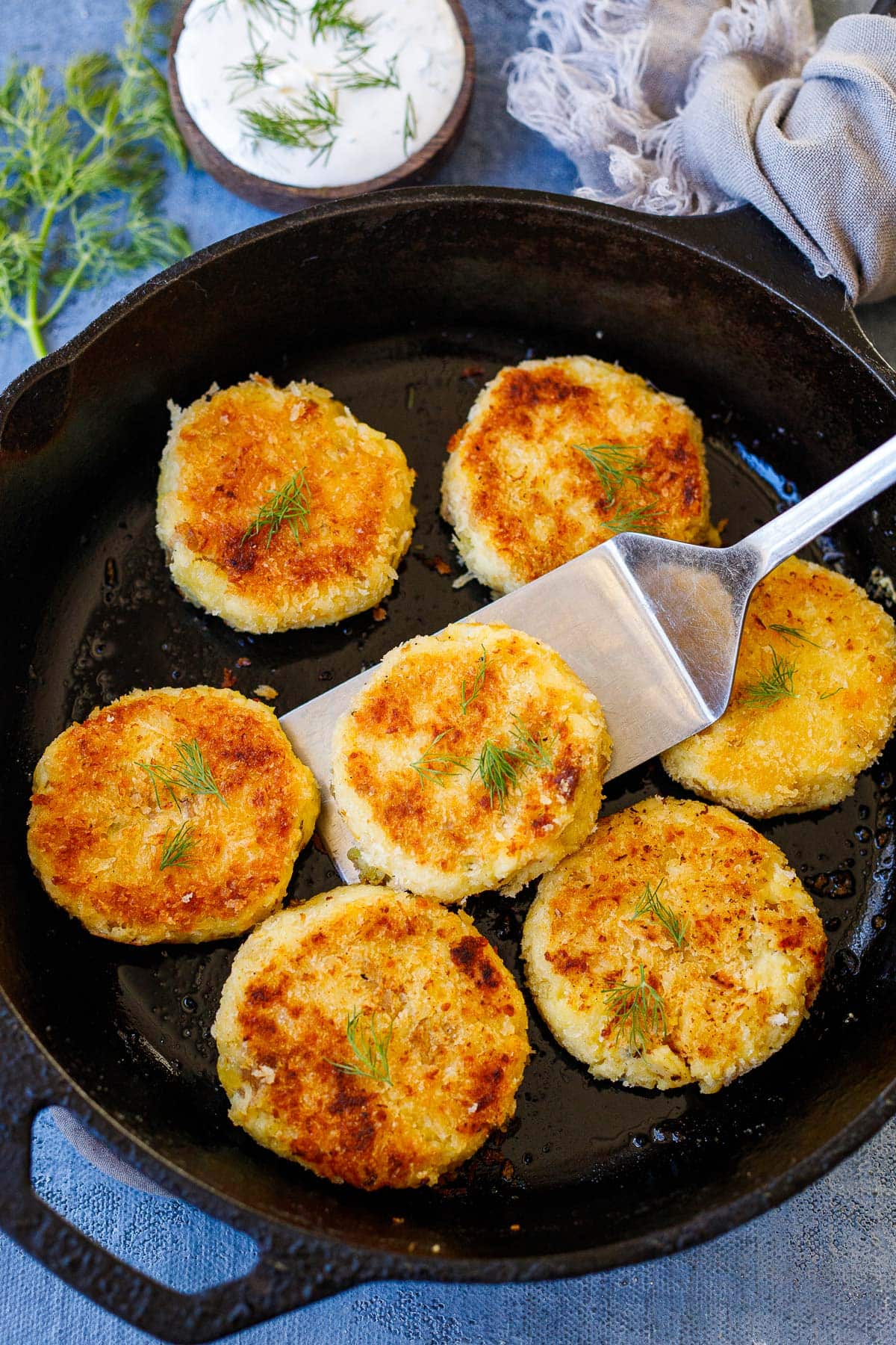 cast iron skillet with spatula holding up mashed potato cakes garnished with fresh dill