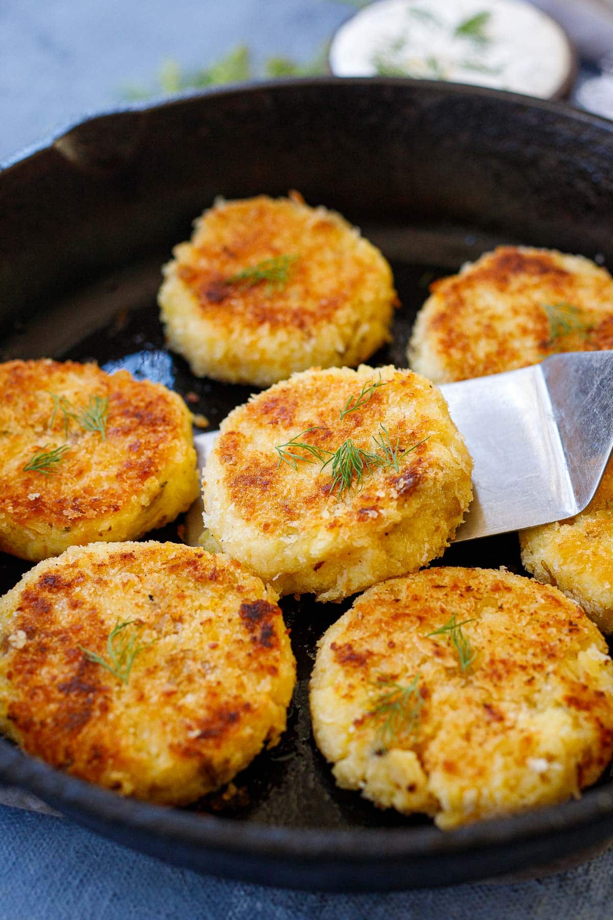 Crispy, mashed potato cakes in a skillet garnished with salt and dill.
