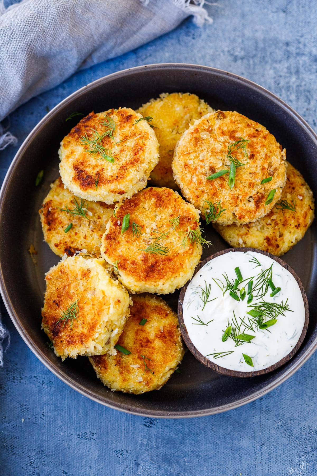 plate with stacked mashed potato cakes garnished with fresh herbs and served with tzatziki sauce
