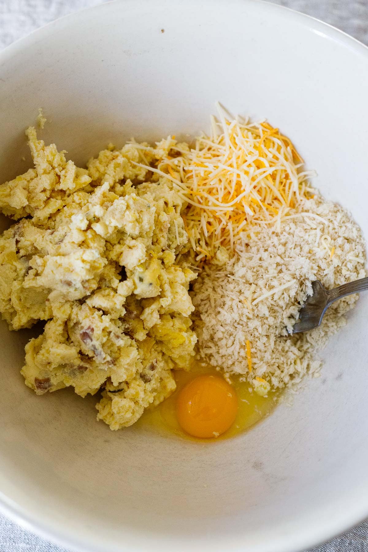 ingredients for mashed potato cakes in mixing bowl - leftover mashed potatoes, grated cheese, panko, egg