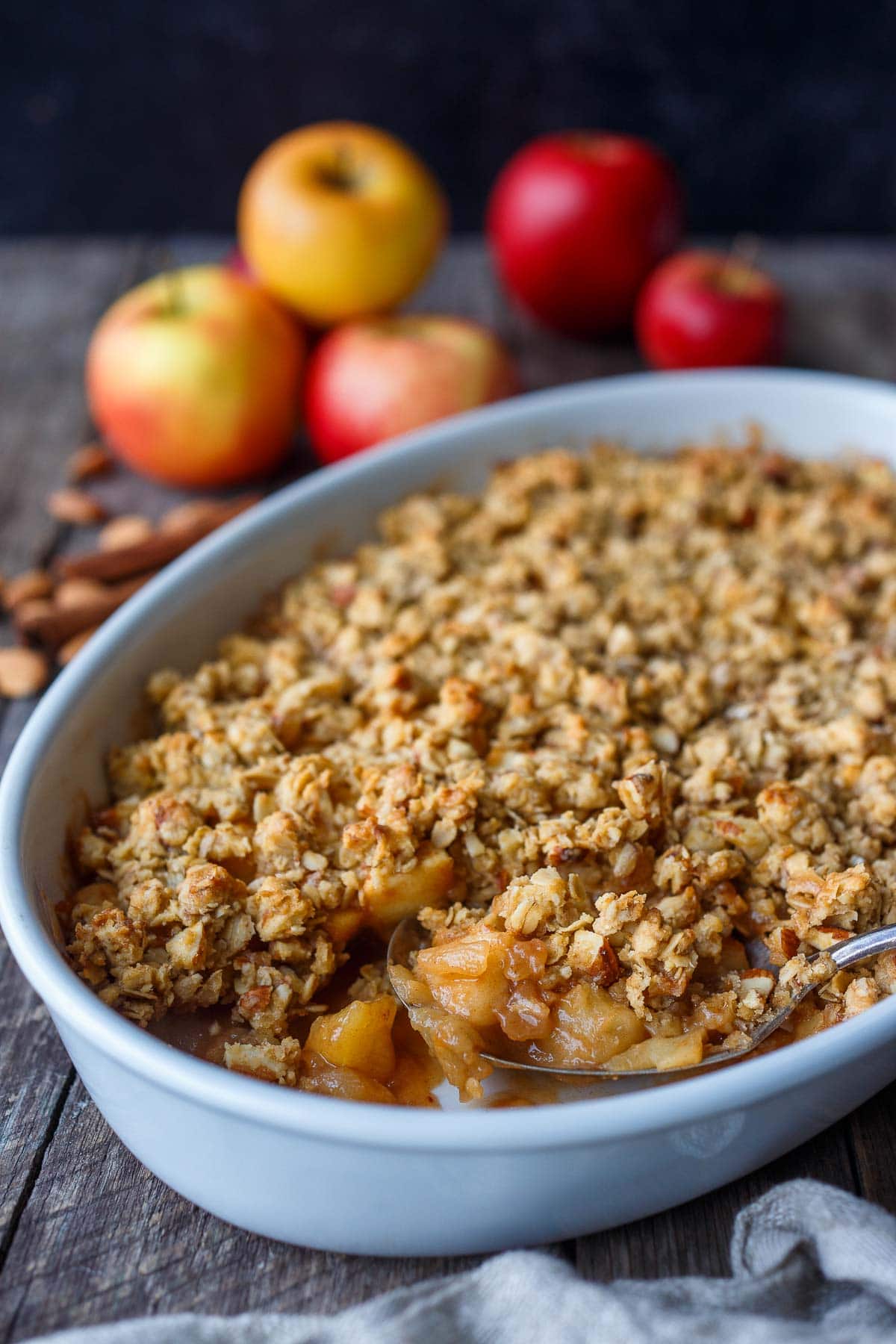 spoonful of apple crisp from dish with cinnamon baked apples topped with oat almond topping