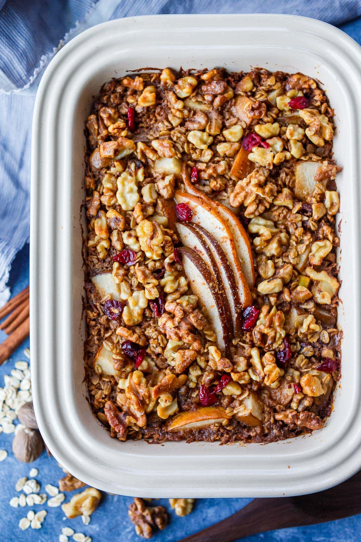baked oatmeal in baking dish topped with walnuts, dried cranberries, and slices of pears