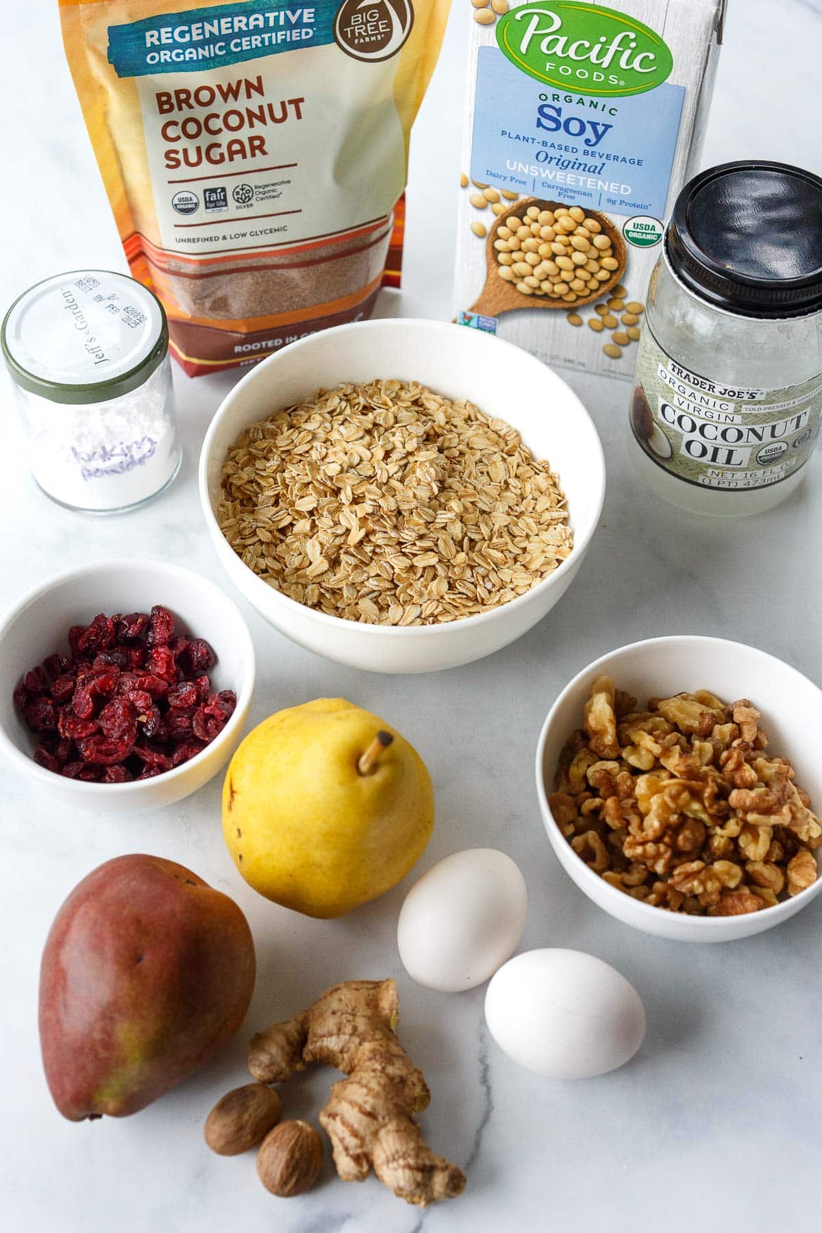 ingredients for baked oatmeal on marble surface - oats, walnuts, dried cranberries, pears, eggs, ginger, baking powder, brown sugar, soy milk, coconut oil