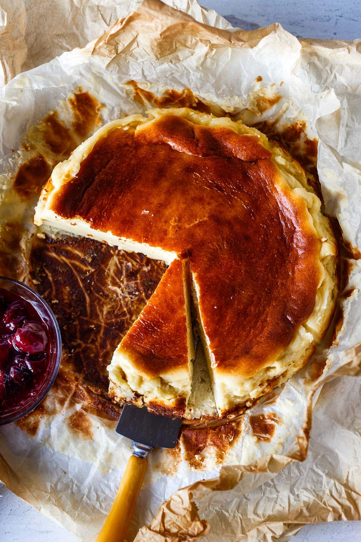 basque cheesecake on crumpled parchment paper, spatula serving slice