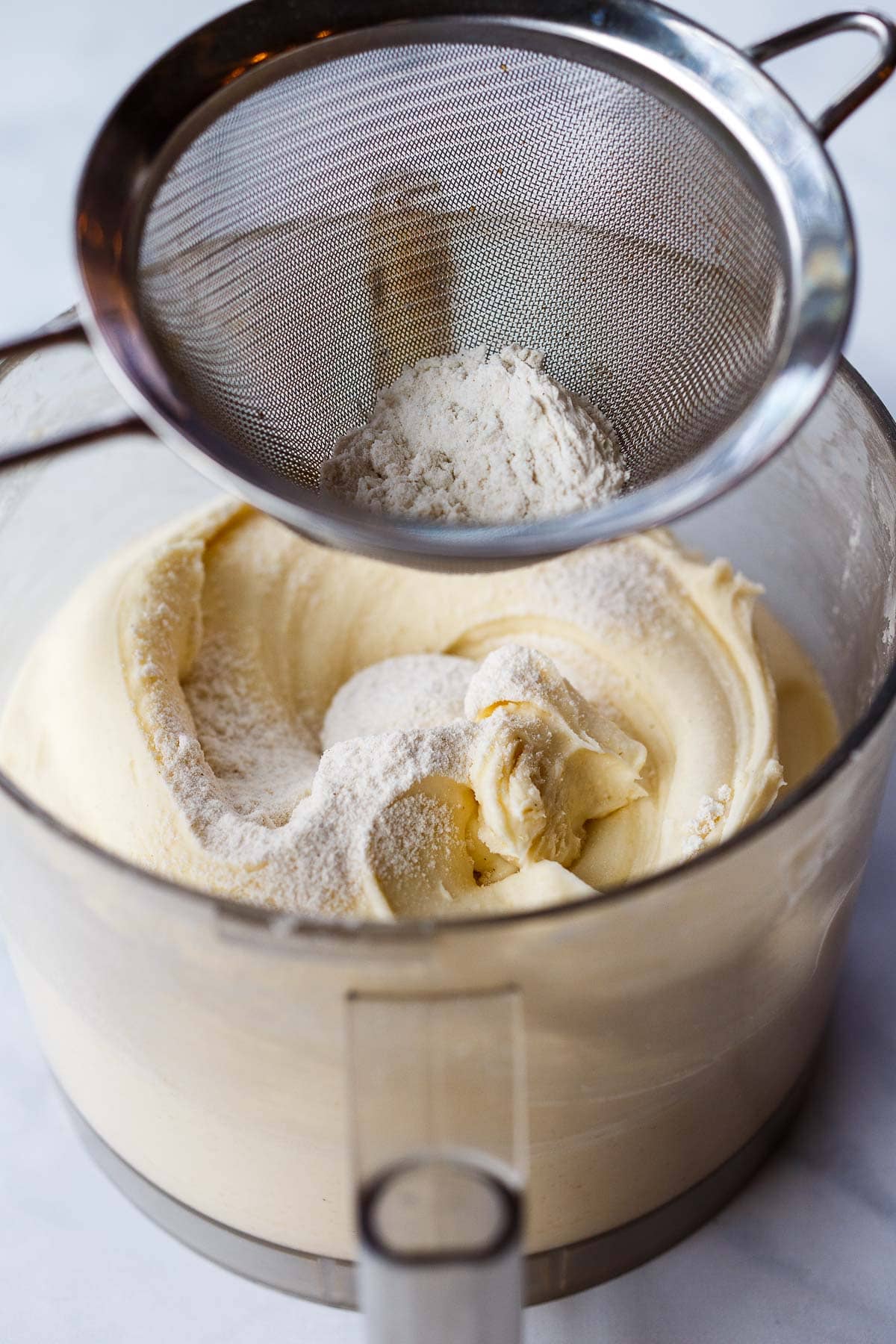 flour sifting into cream cheese mixture in food processor