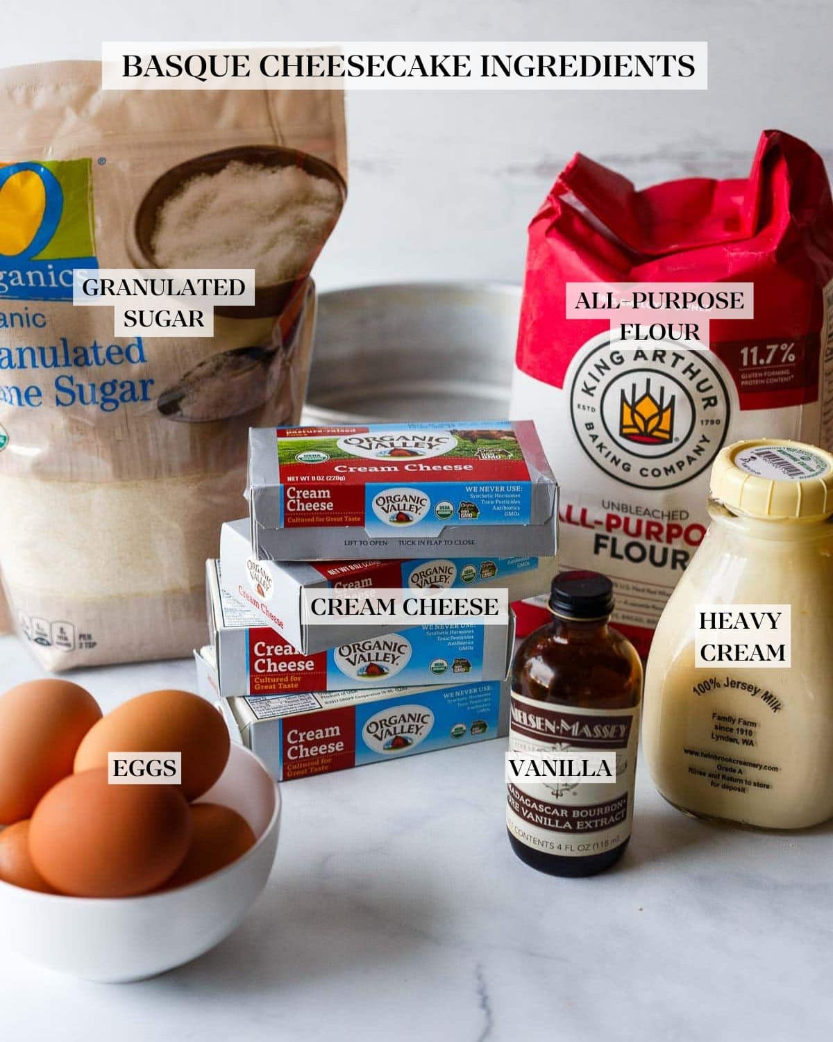 basque cheesecake ingredients on marble counter - cane sugar, all purpose flour, milk, vanilla, cream cheese, eggs.