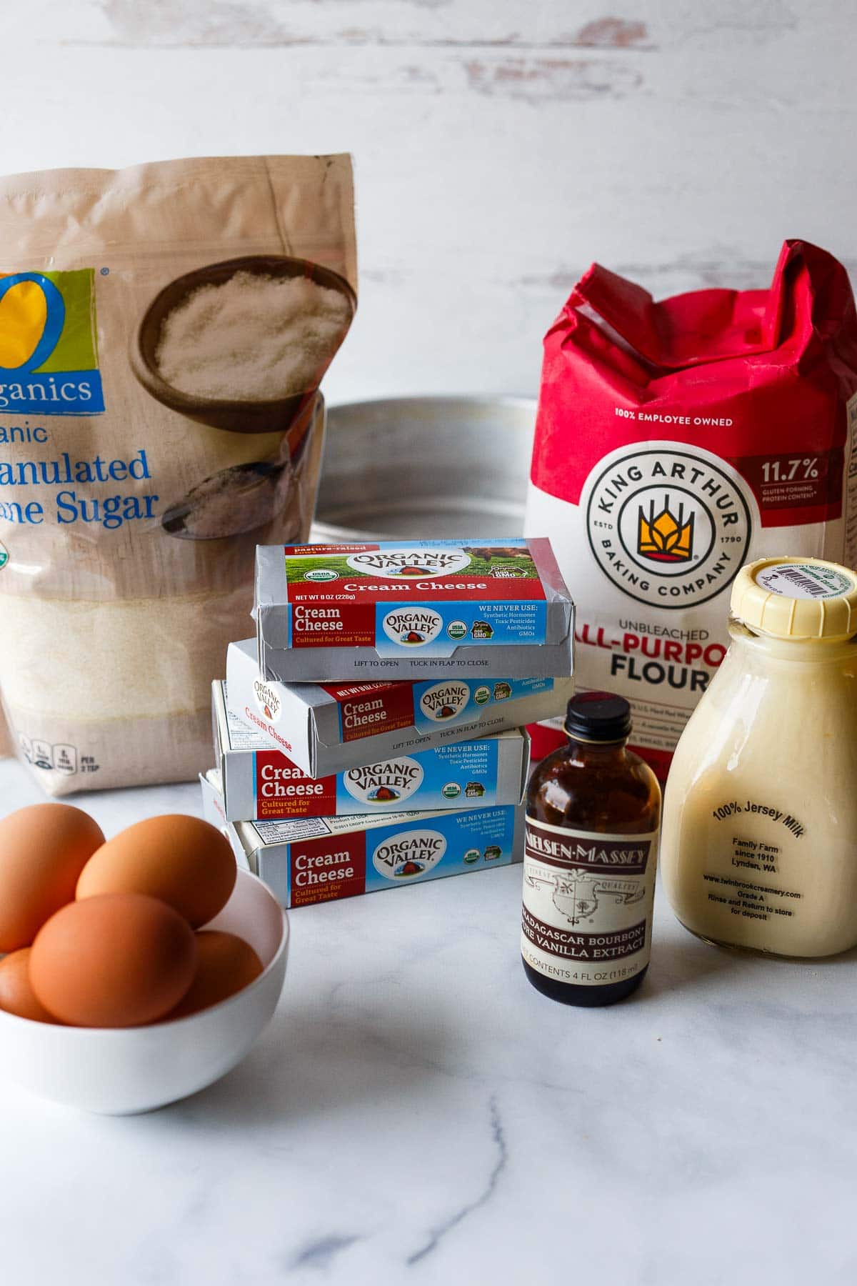 basque cheesecake ingredients on marble counter - cane sugar, all purpose flour, milk, vanilla, cream cheese, eggs