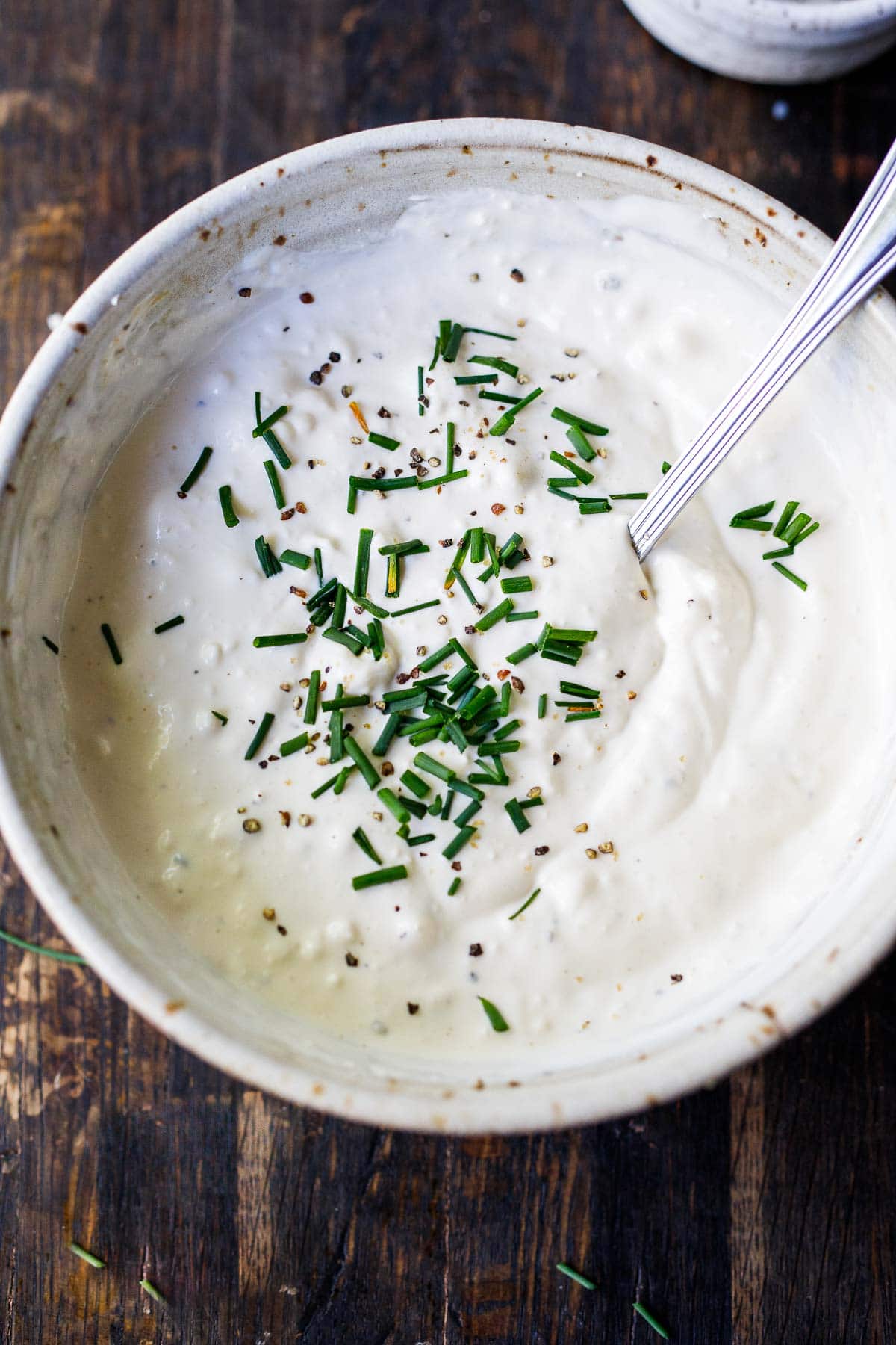 blue cheese dressing in bowl with spoon, garnished with black pepper and fresh chives