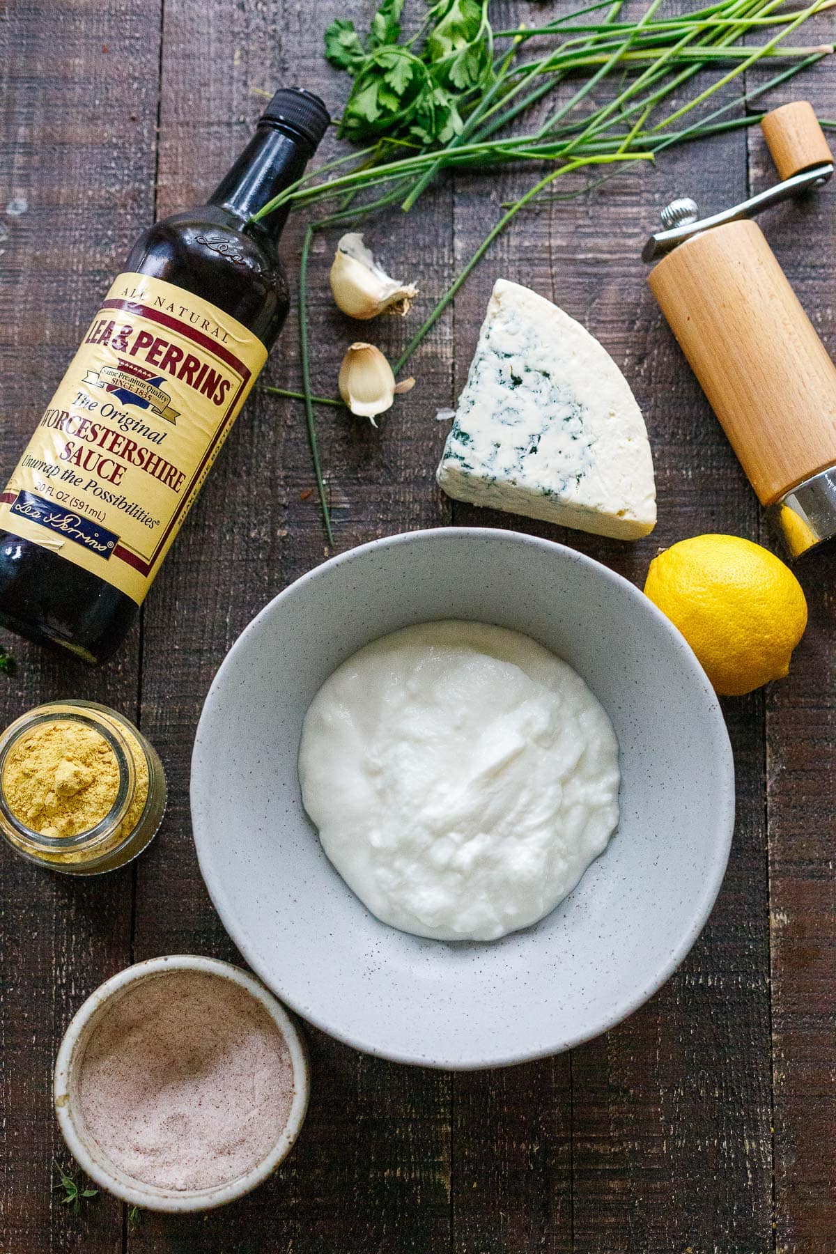 ingredients for blue cheese dressing on wood surface - blue cheese, yogurt, lemon, garlic, dried mustard, pepper shaker, worcestershire, salt