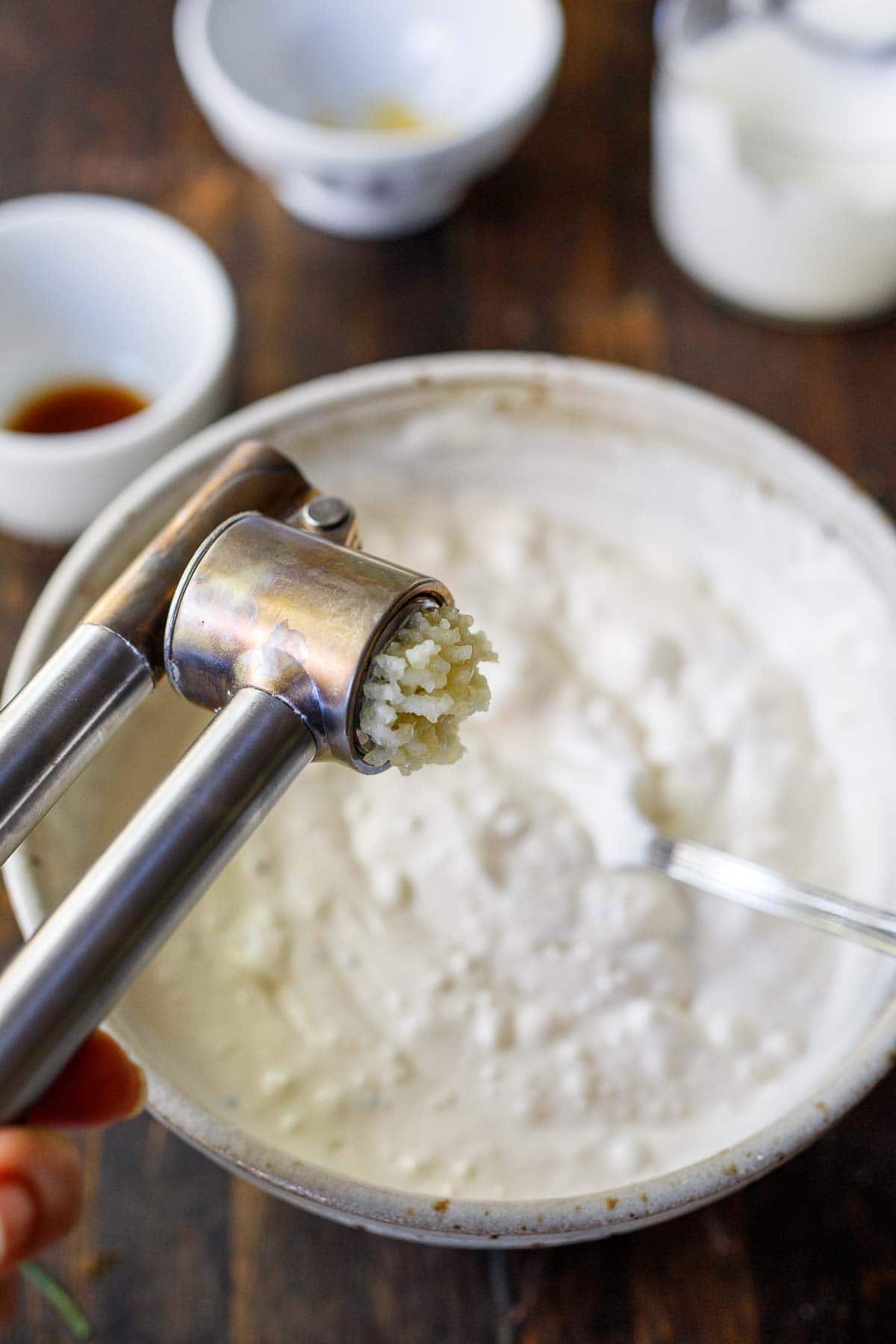 garlic press crushing garlic into bowl of blue cheese dressing