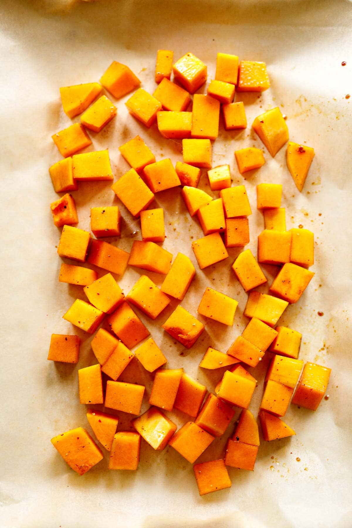 cubed butternut squash spread out on parchment-lined sheet pan with oil and spices
