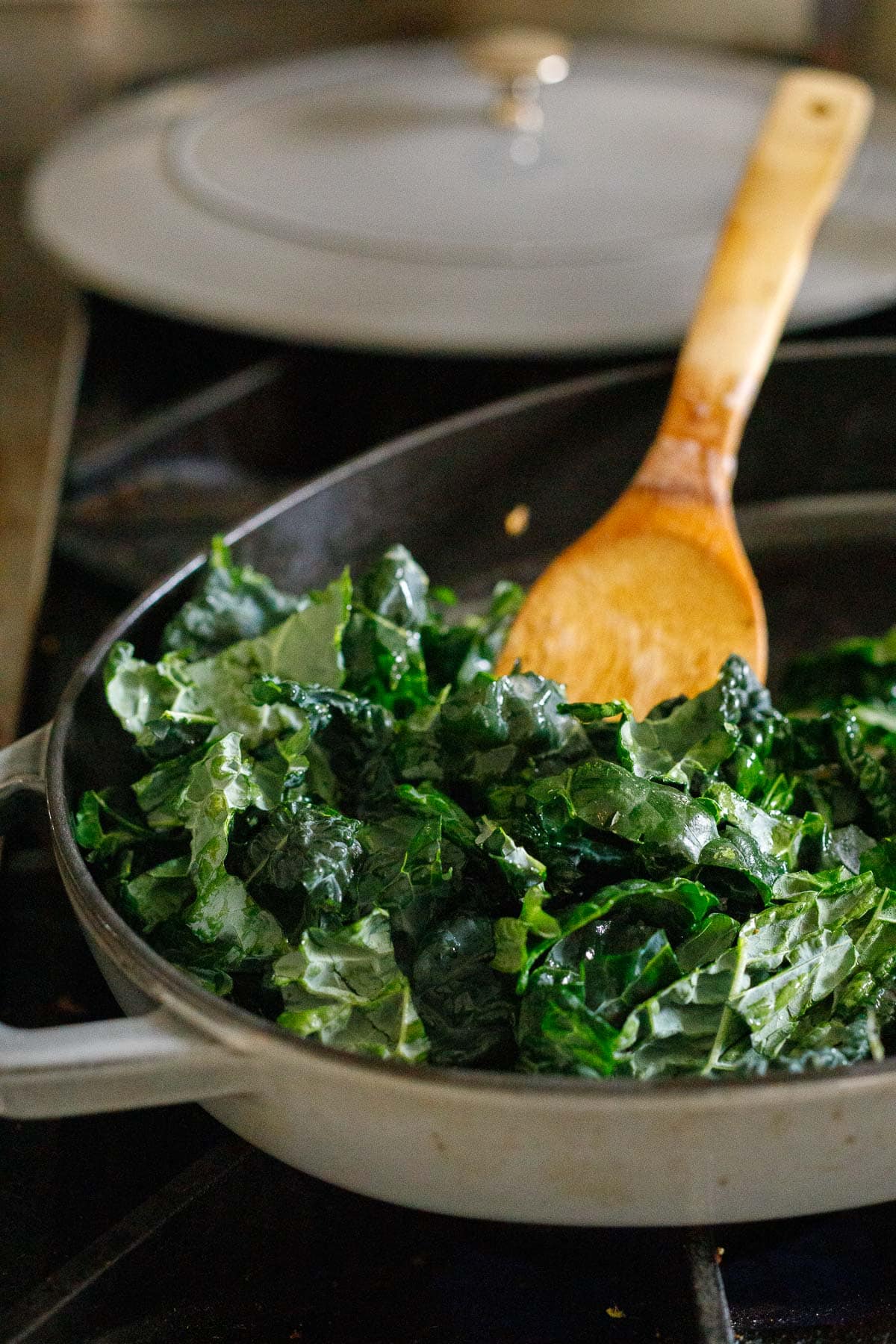 large skillet with kale wilting in pan with spatula