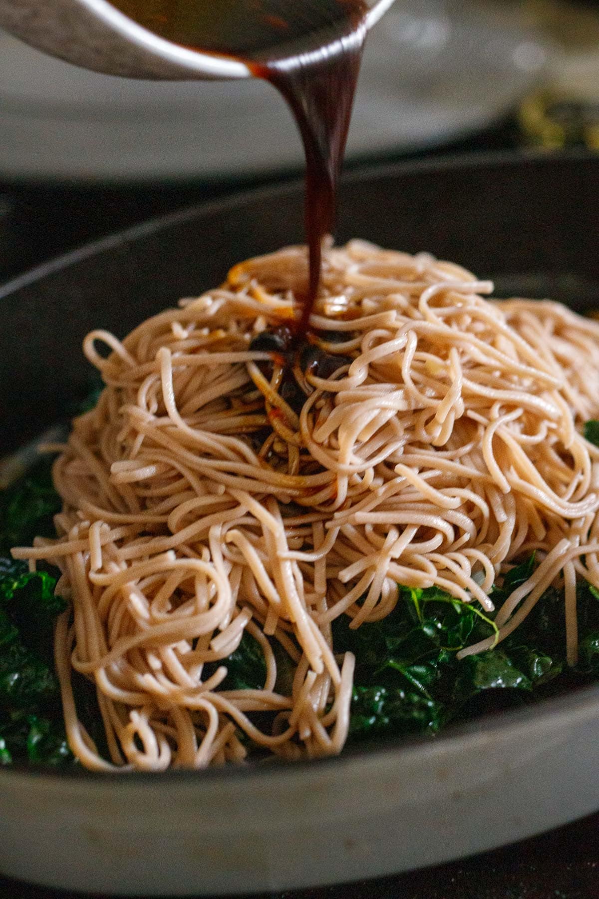 soba noodles added to large skillet with wilted kale and stir fry sauce poured over top