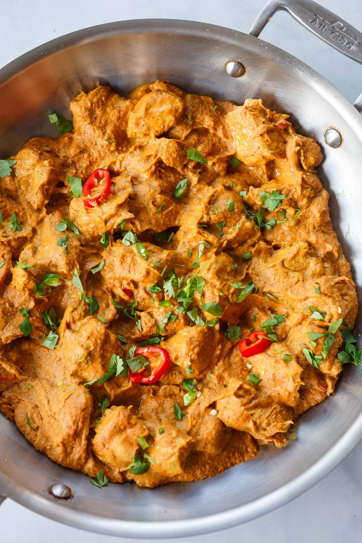 chicken korma with thick and creamy sauce simmering in skillet, garnished with sliced chilies and fresh herbs
