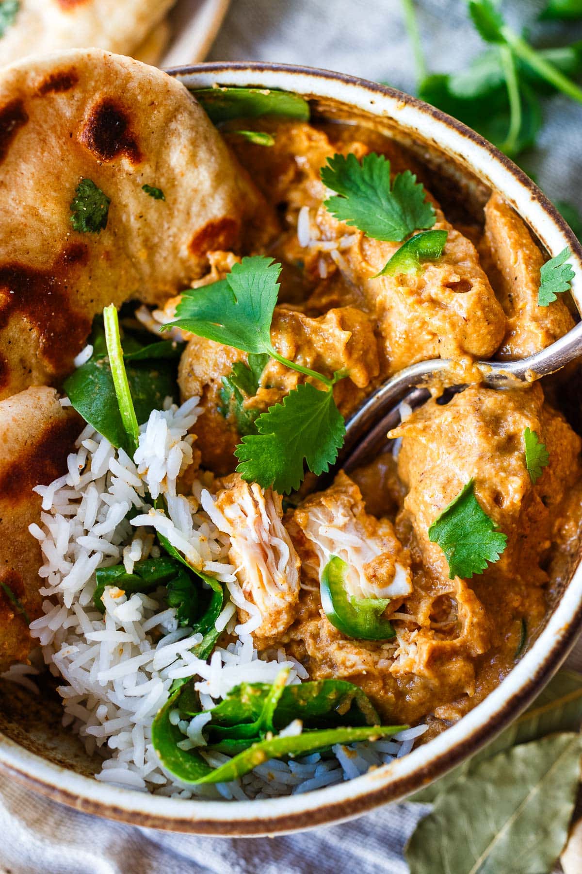 chicken korma in bowl with cilantro, spinach, and naan