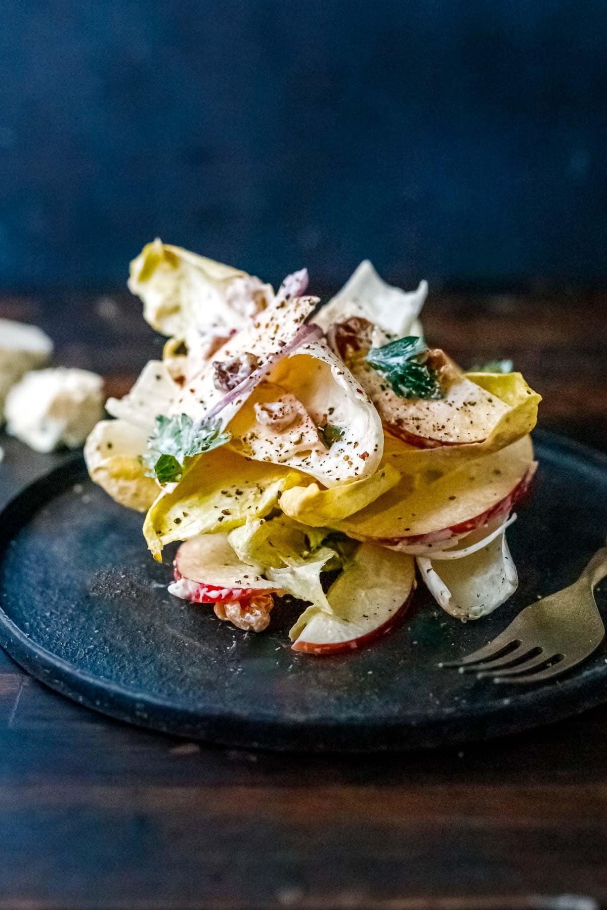 endive salad stacked on plate with blue cheese dressing, apples, red onion, toasted walnuts, parsley, black pepper.