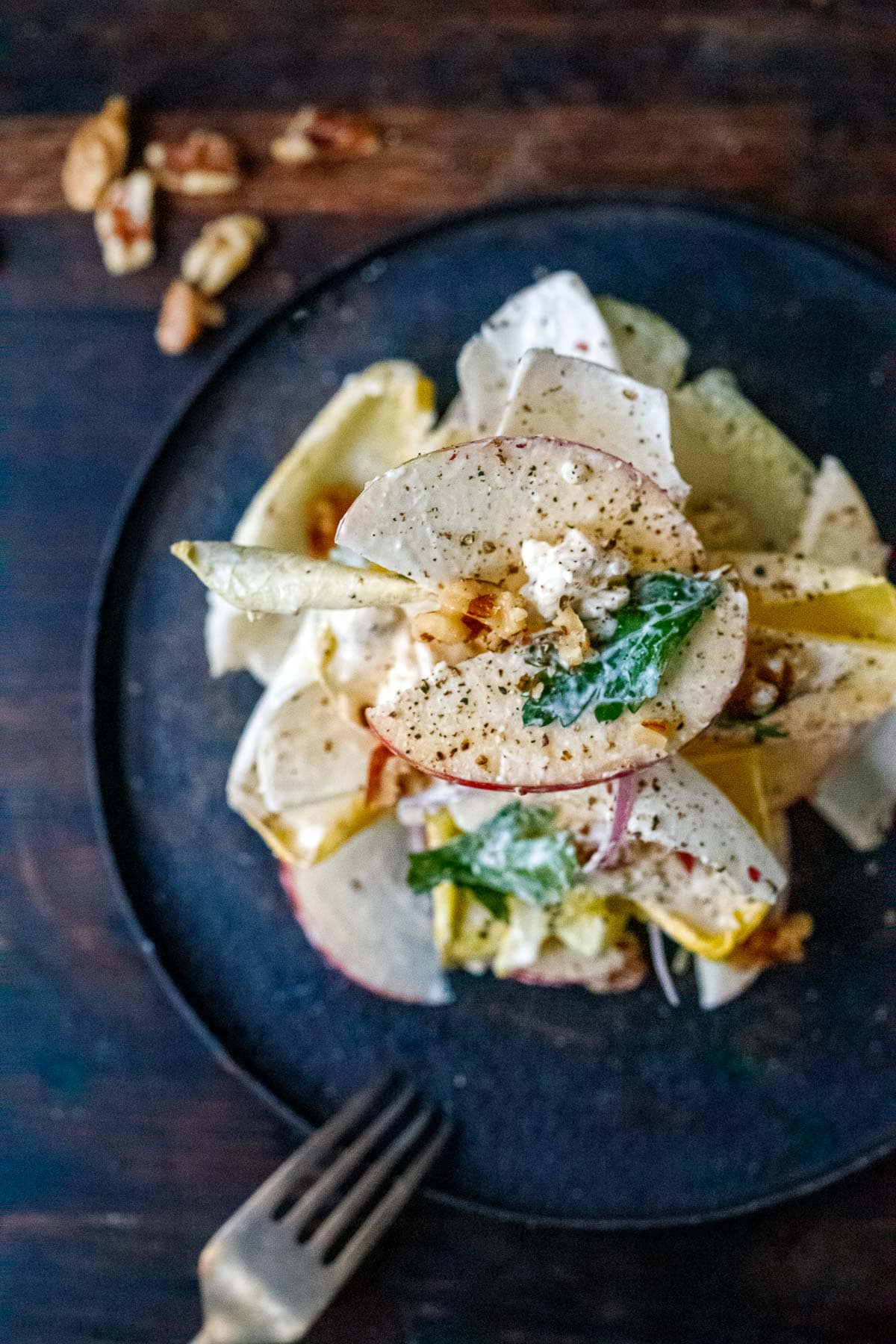 overhead of endive salad with blue cheese dressing stacked on plate with sliced apples, parsley, toasted walnuts, cracked pepper