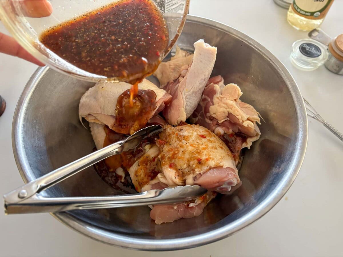 pouring szechuan marinade over a bowl of chicken thighs with tongs.
