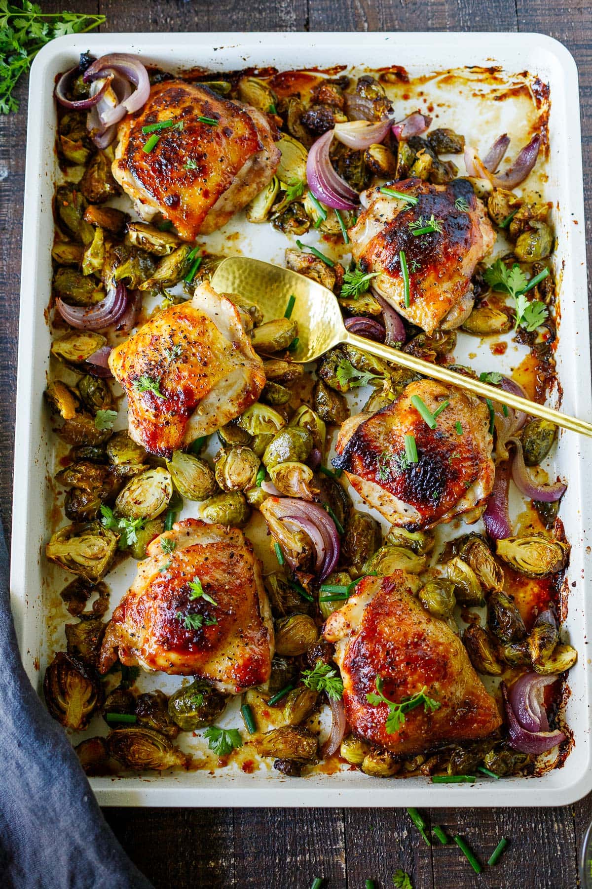 sheet pan chicken with brussels sprouts and onions with gold serving spoon.