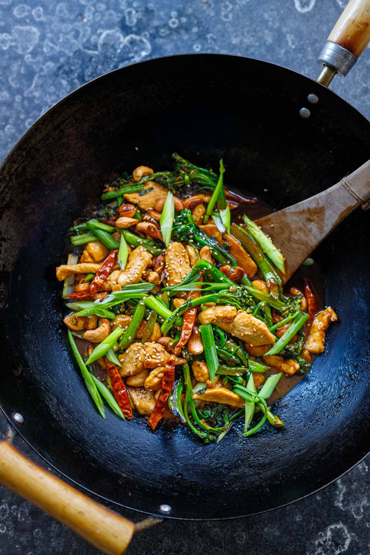 szechuan chicken stir fry in wok with broccolini, green onions, toasted cashews, sesame seeds, chilies