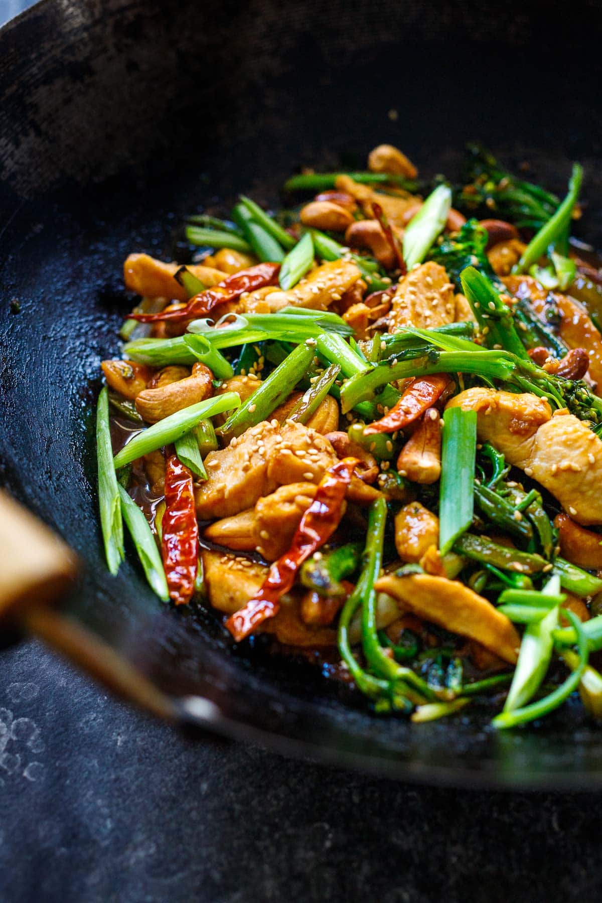 szechuan chicken stir fry in wok with broccolini, scallions, sesame seeds, dried chilies, toasted cashews