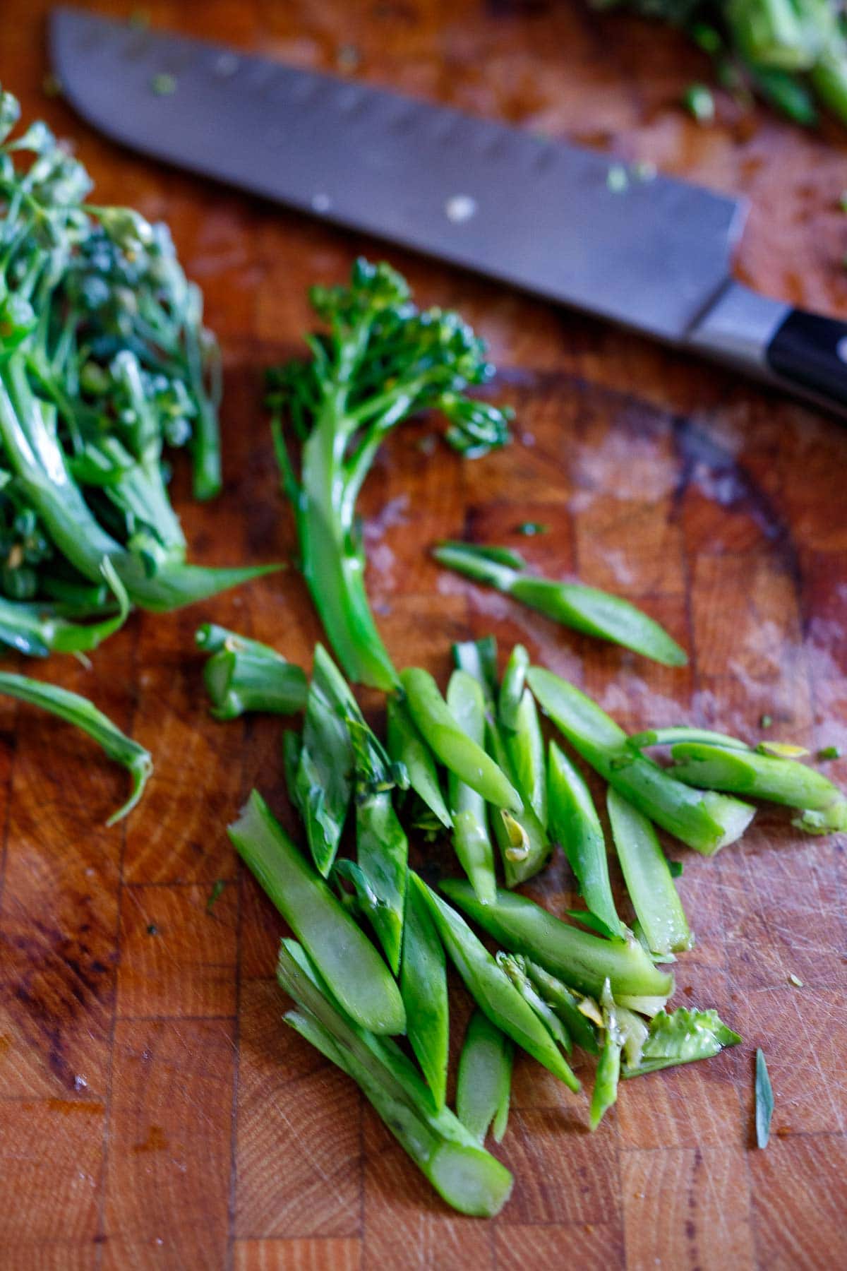 chef's knife on cutting board with sliced broccolini