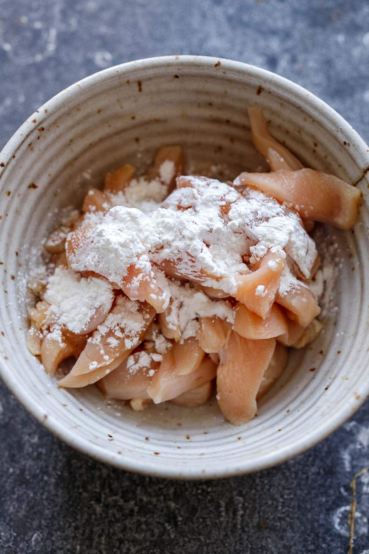 thinly sliced chicken in bowl with cornstarch